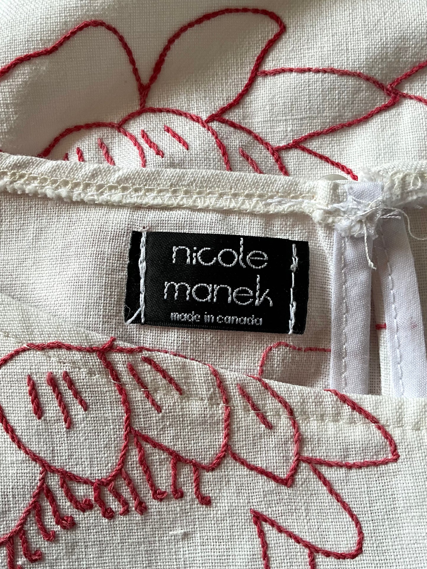 Textile with embroidered design and 'nicole manek' label on a white background