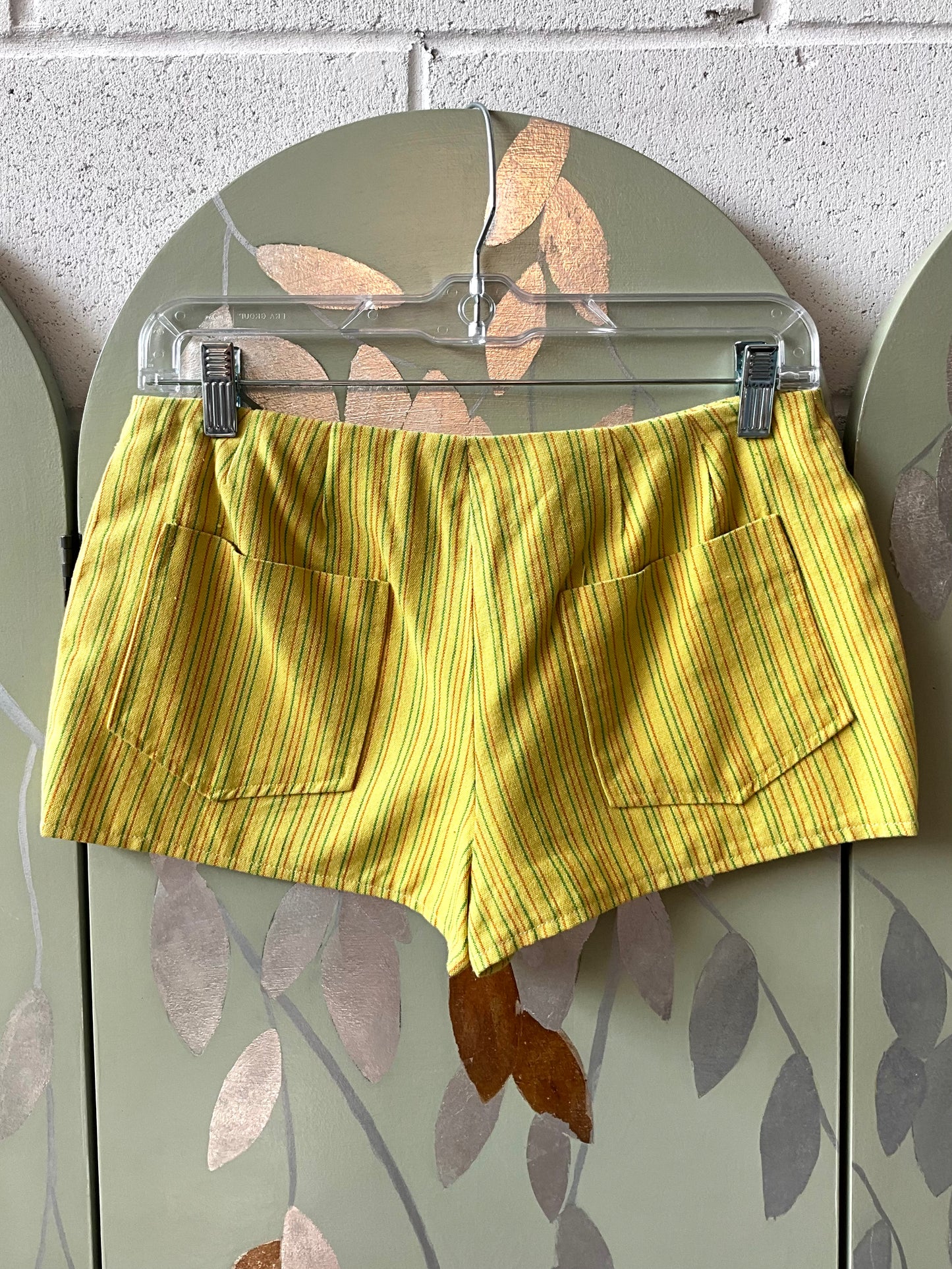 Yellow striped shorts on a hanger against a wall.