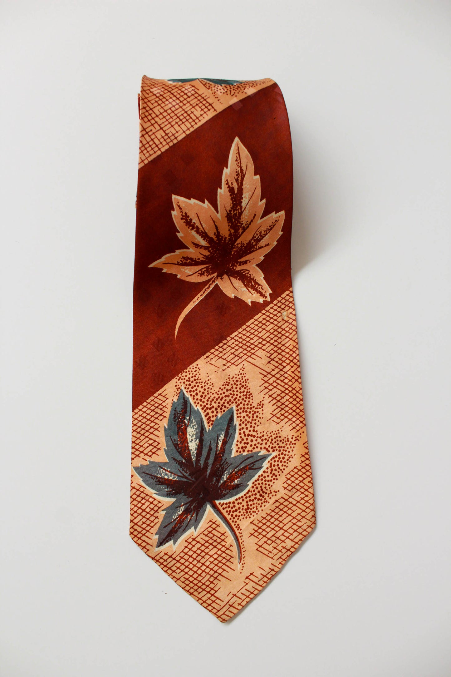 1940s brown and green leaf print necktie against tan and brown check background, wide tongue bold look vintage tie