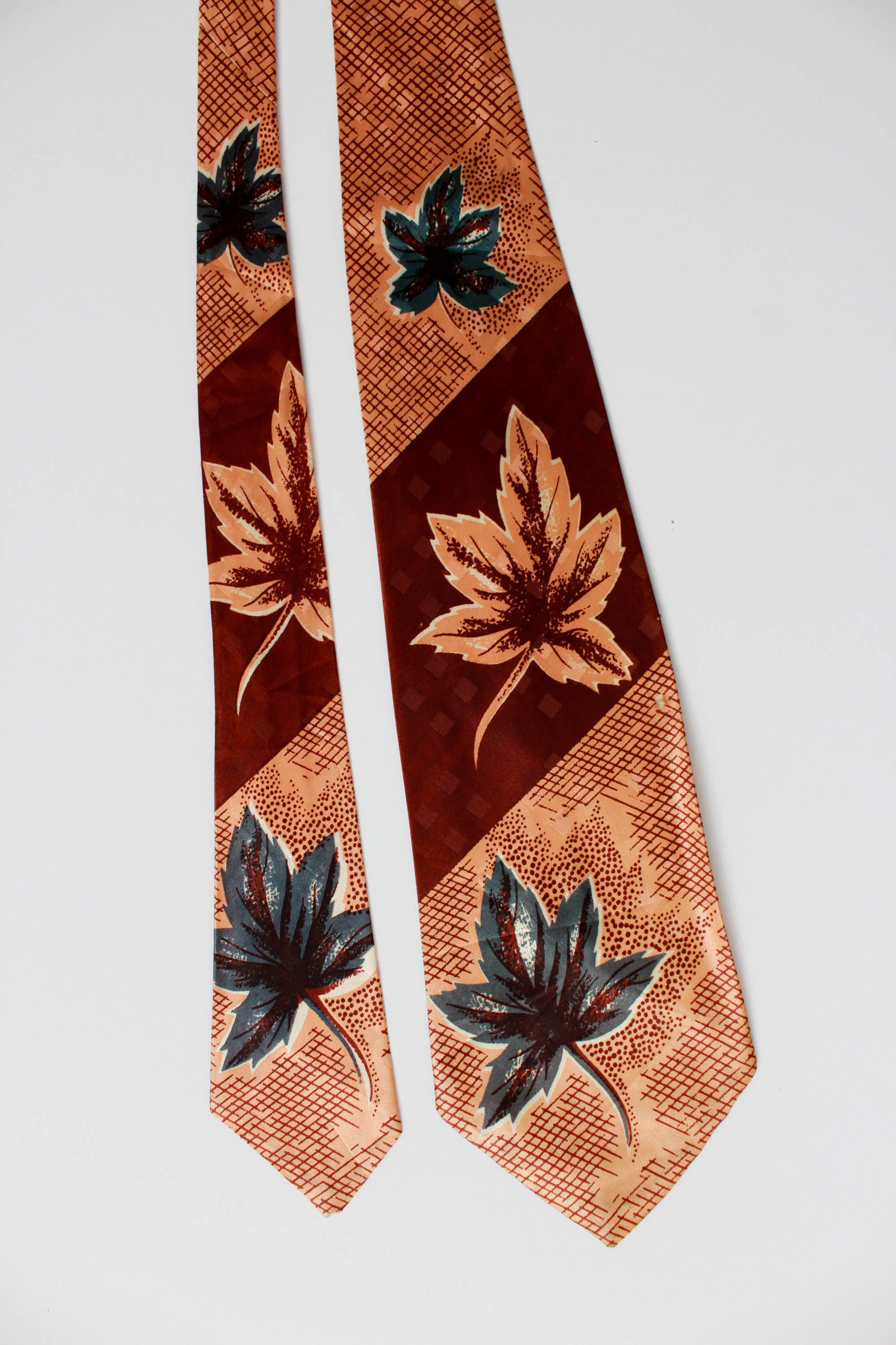 1940s brown and green leaf print necktie against tan and brown check background, wide tongue bold look vintage tie