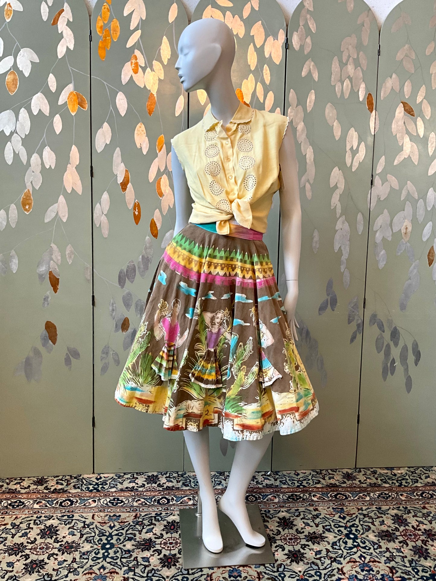 Mannequin wearing a yellow top and patterned skirt against a decorative wall.