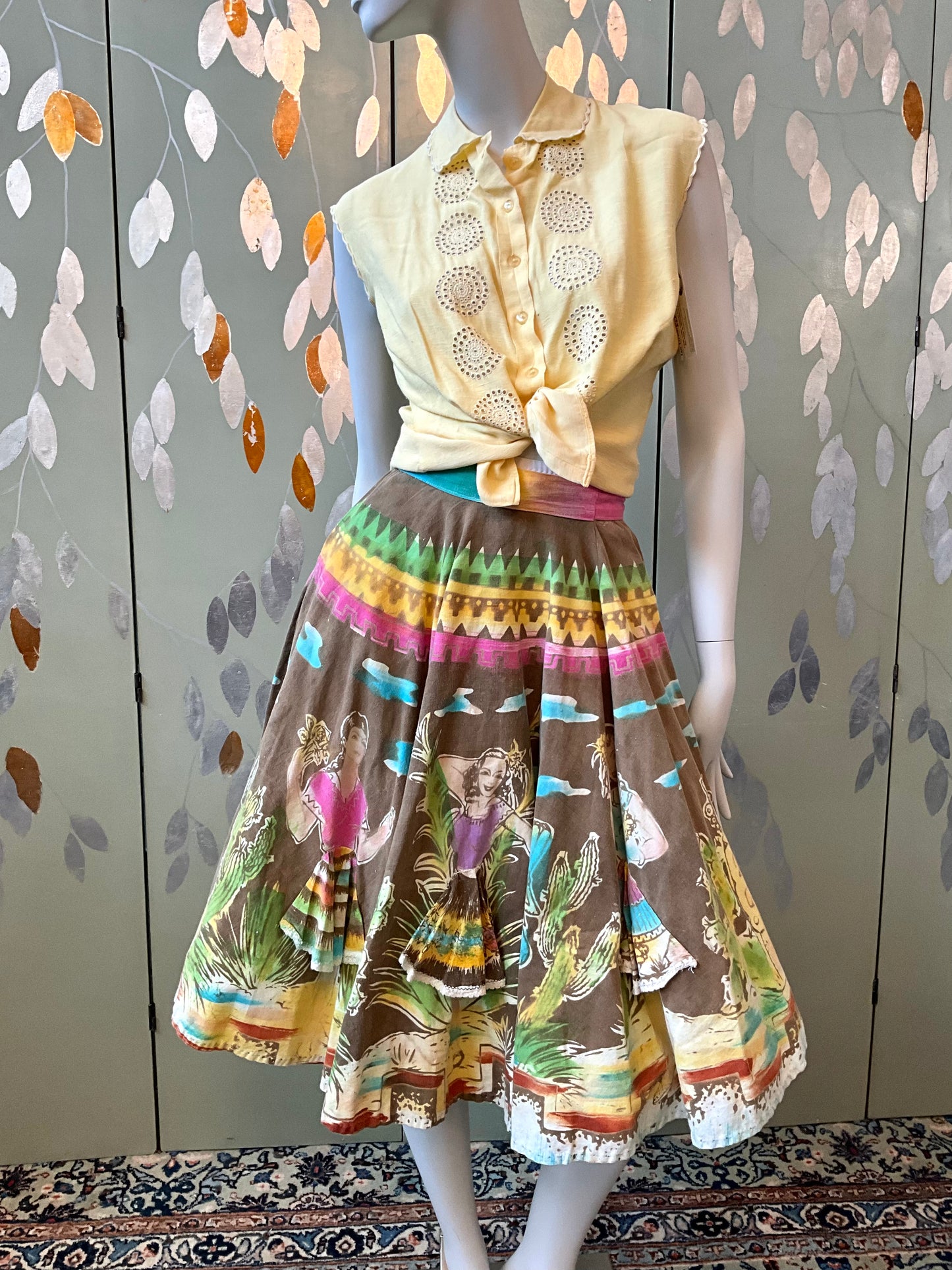 Mannequin wearing a vintage outfit with a colorful skirt and yellow top against a patterned wall.