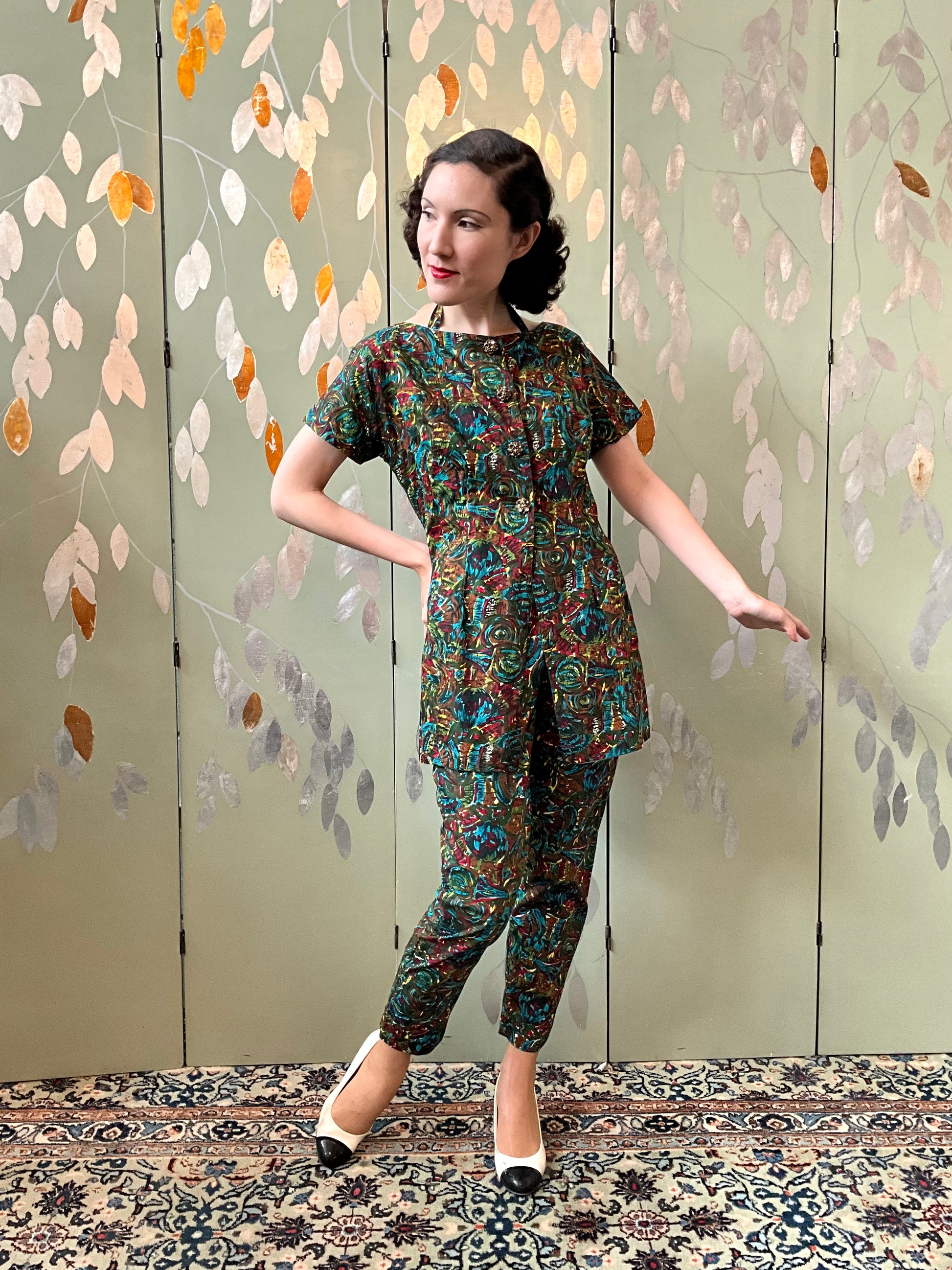 Woman in a patterned outfit standing in front of a decorative wall with leaf patterns.