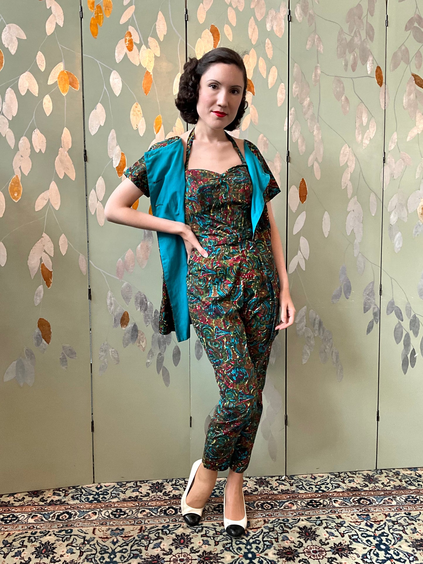 Woman in a patterned outfit standing against a decorative wall with leaf designs.