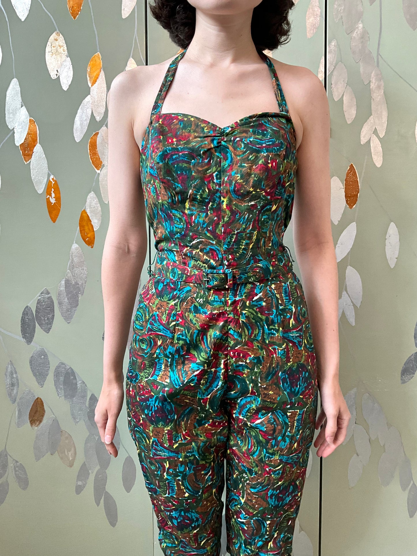 Person wearing a colorful patterned jumpsuit against a leafy background