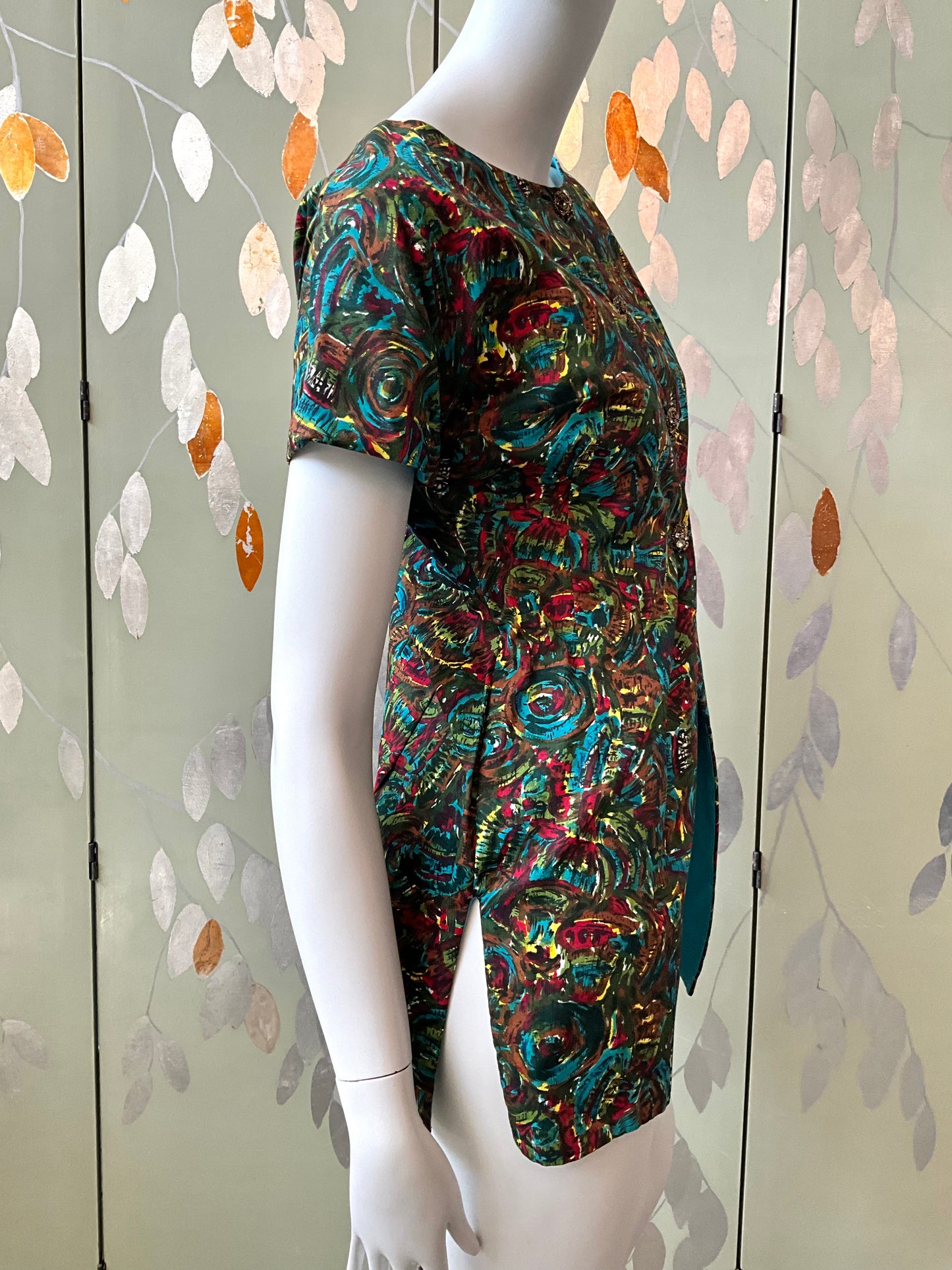 Mannequin wearing a colorful patterned top against a decorative wall.