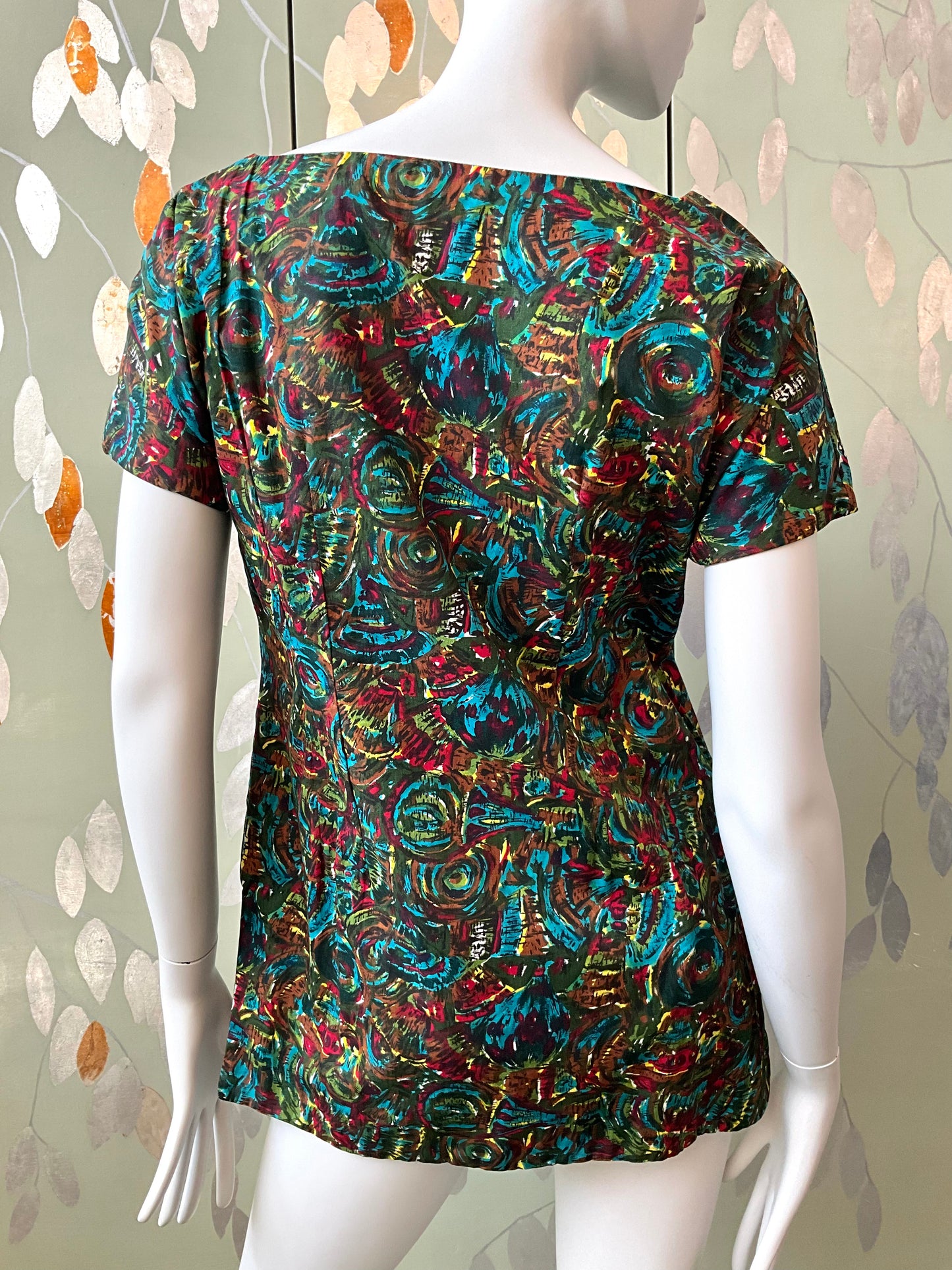 Mannequin wearing a colorful patterned top against a leafy background