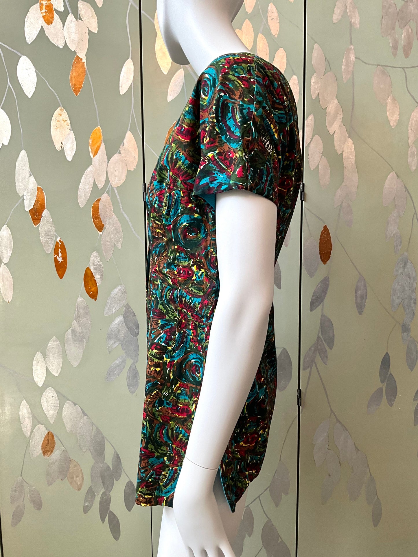 Mannequin wearing a colorful patterned top against a decorative wall.