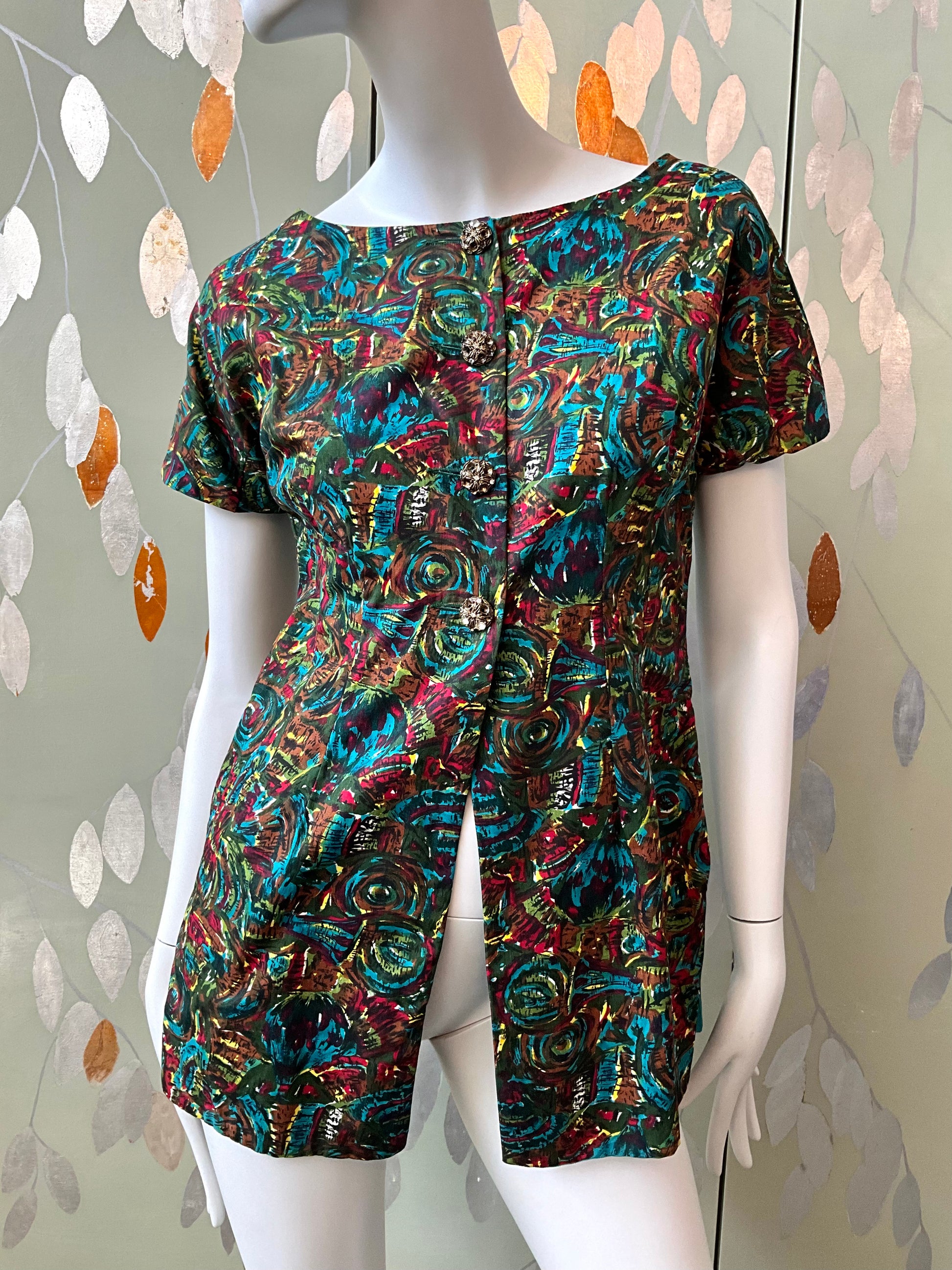 Mannequin wearing a colorful patterned top against a decorative wall.