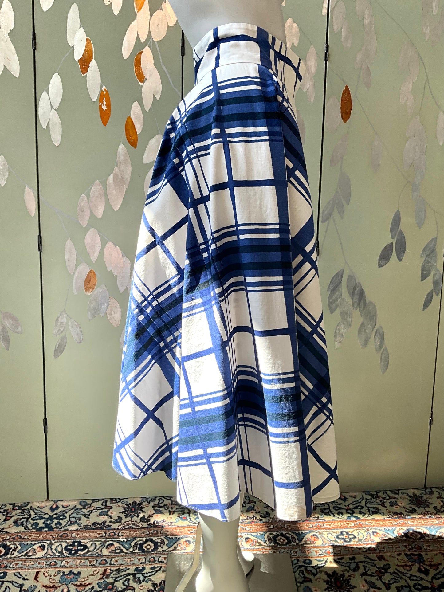 Mannequin wearing a blue and white plaid skirt against a decorative wall.