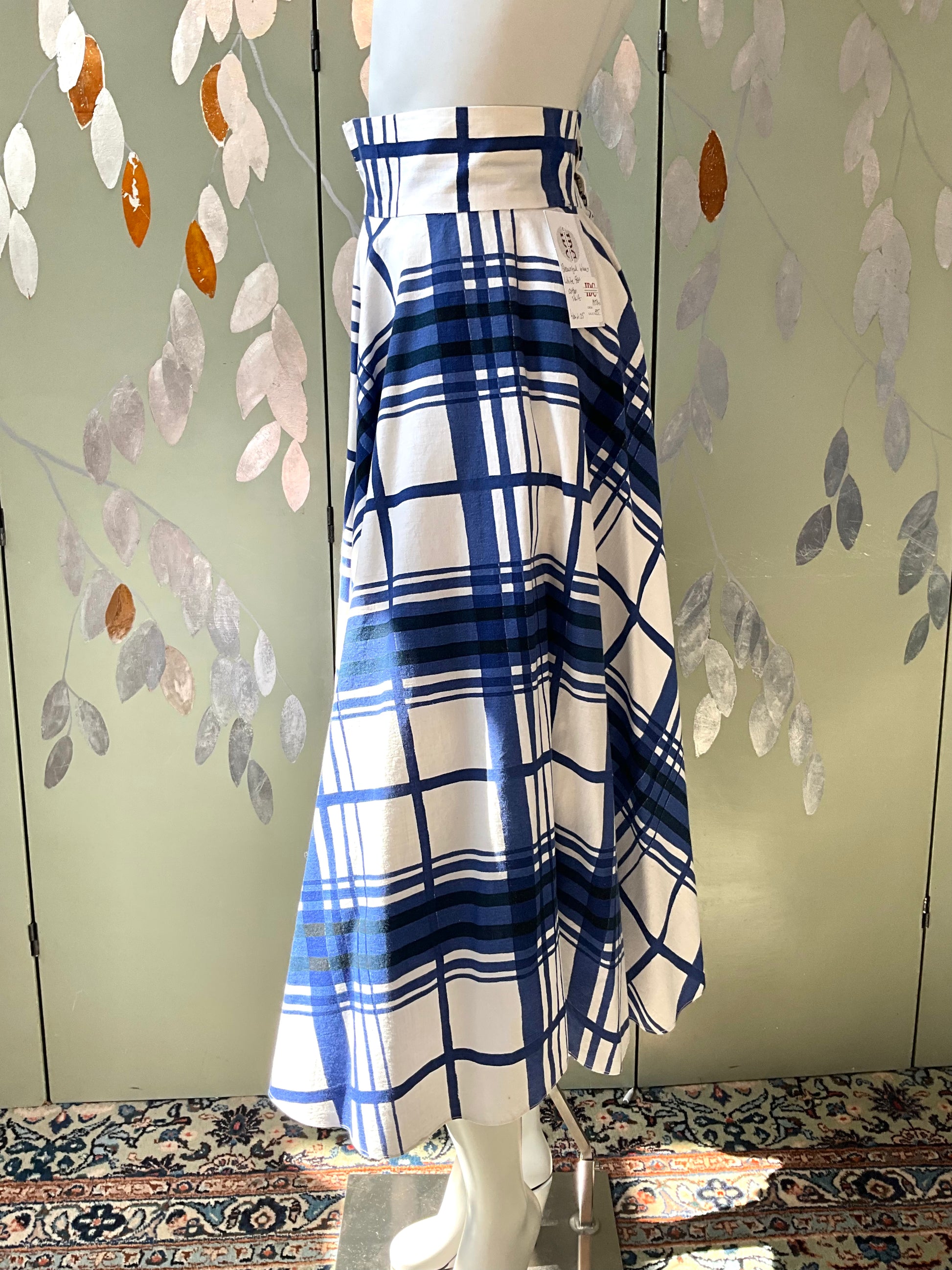 Mannequin wearing a blue and white plaid skirt against a decorative wall.