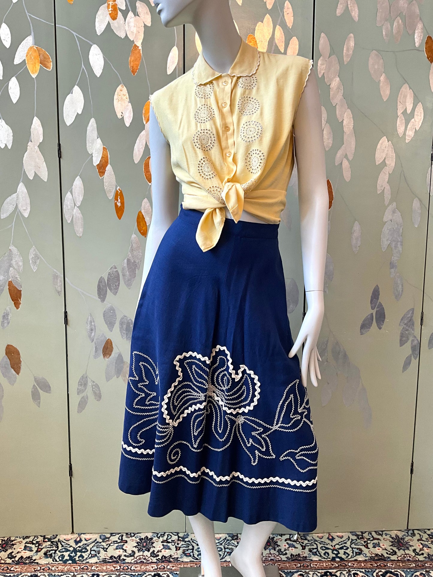 Mannequin wearing a yellow top and blue skirt with floral patterns against a decorative wall.