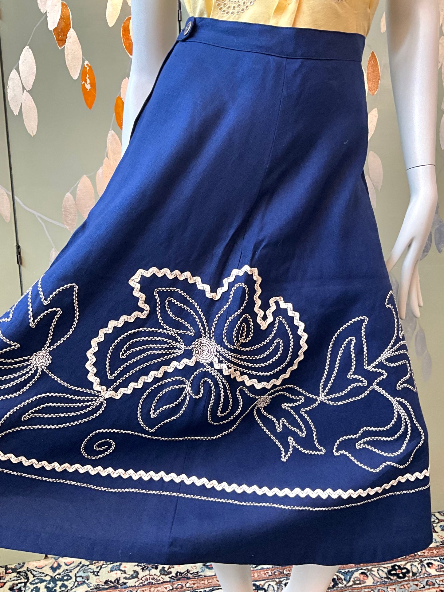 Blue skirt with white floral embroidery on a mannequin against a patterned background