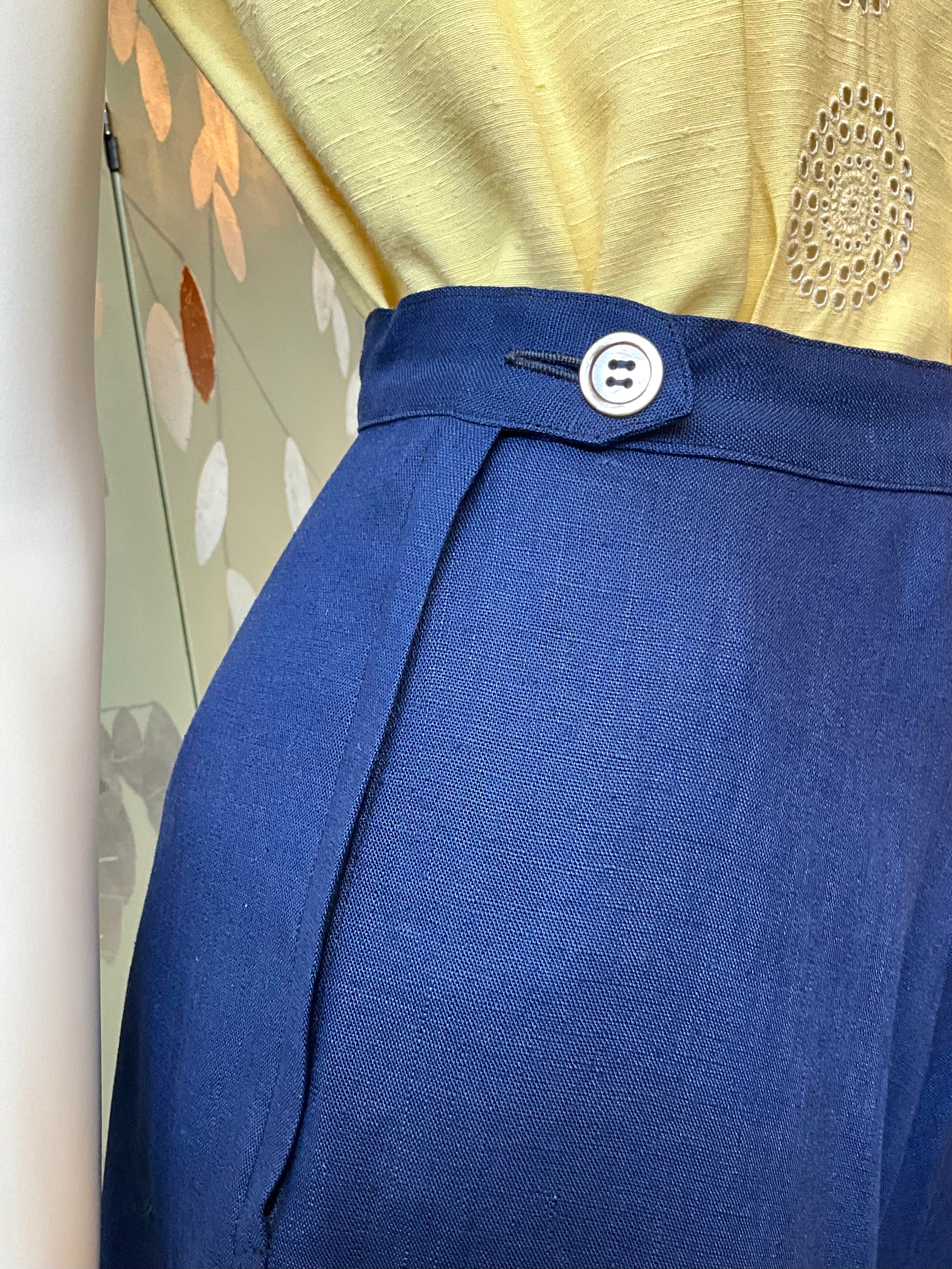 Close-up of a blue skirt with a button on a mannequin against a floral background