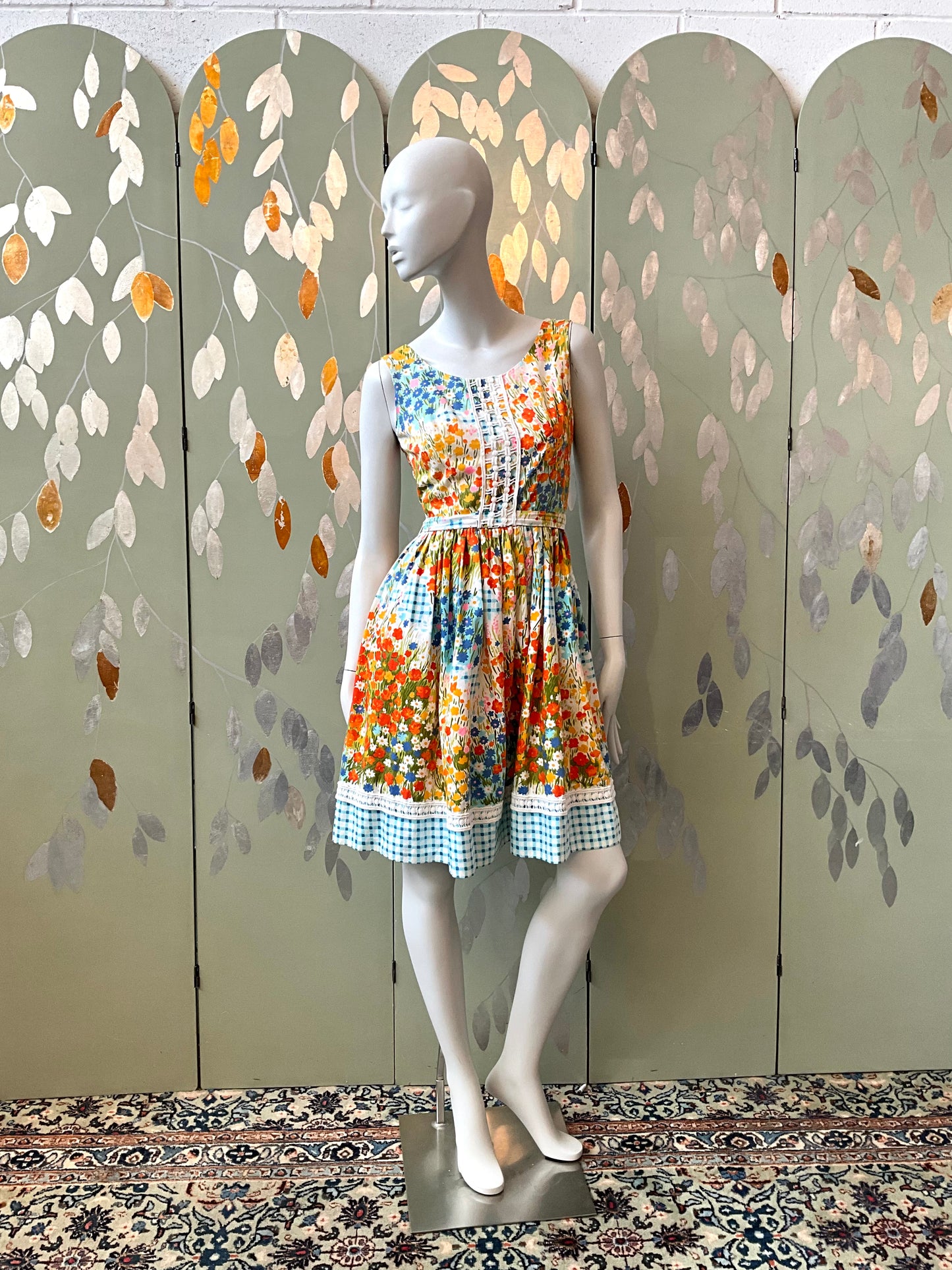 Mannequin wearing a colorful dress in front of a decorative screen with leaf patterns.