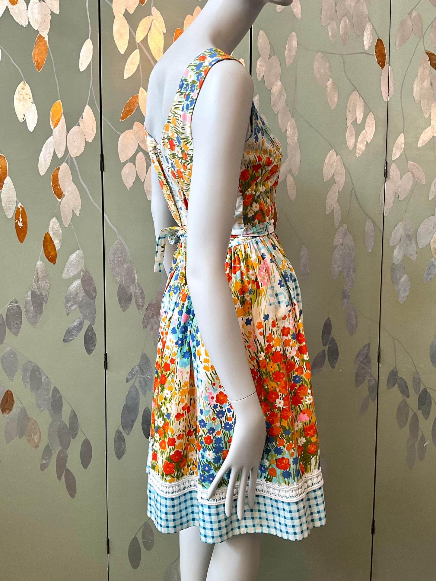 Mannequin wearing a colorful floral dress against a decorative wall with leaf patterns.