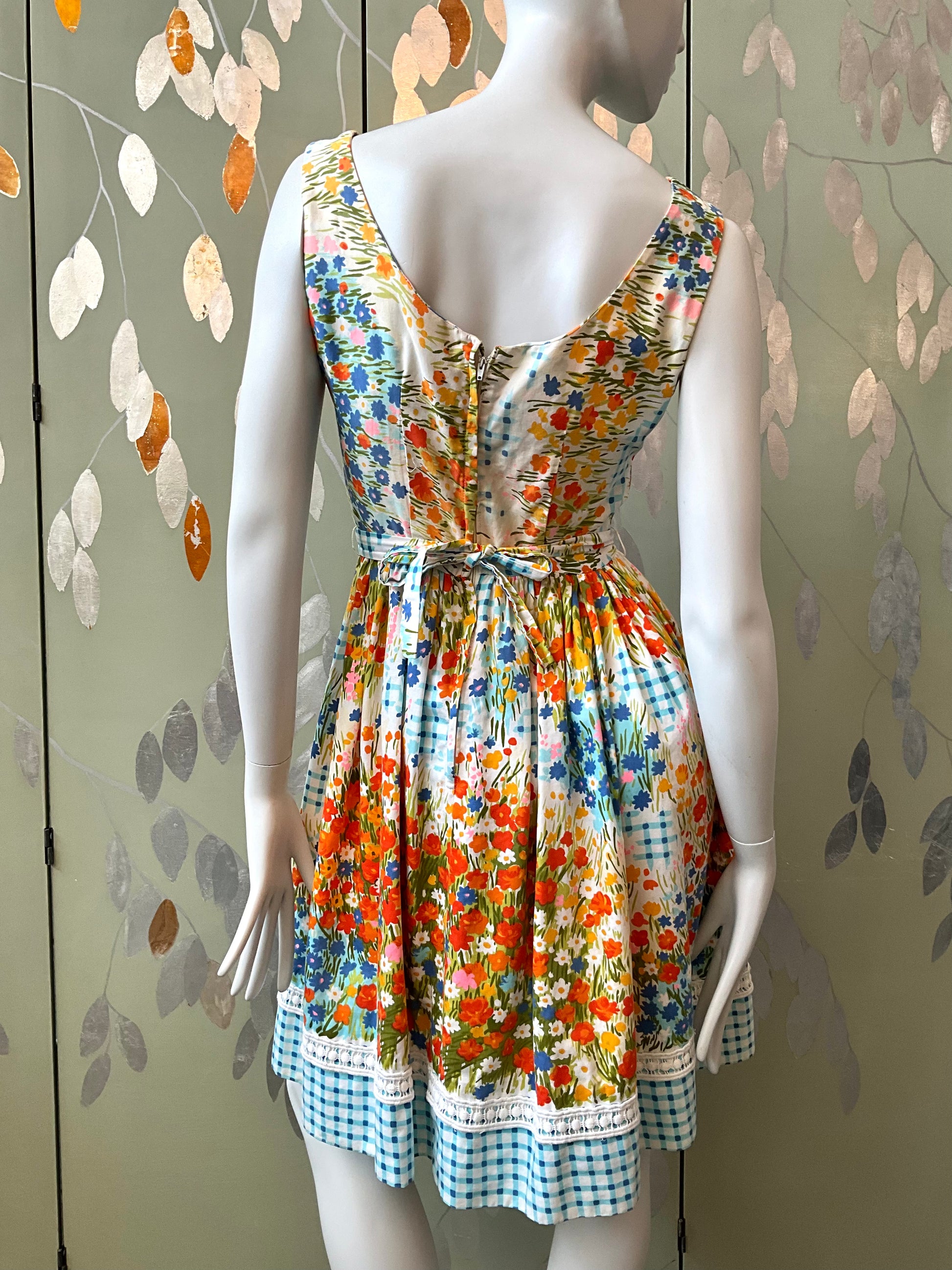 Mannequin wearing a colorful floral dress against a leaf-patterned wall.
