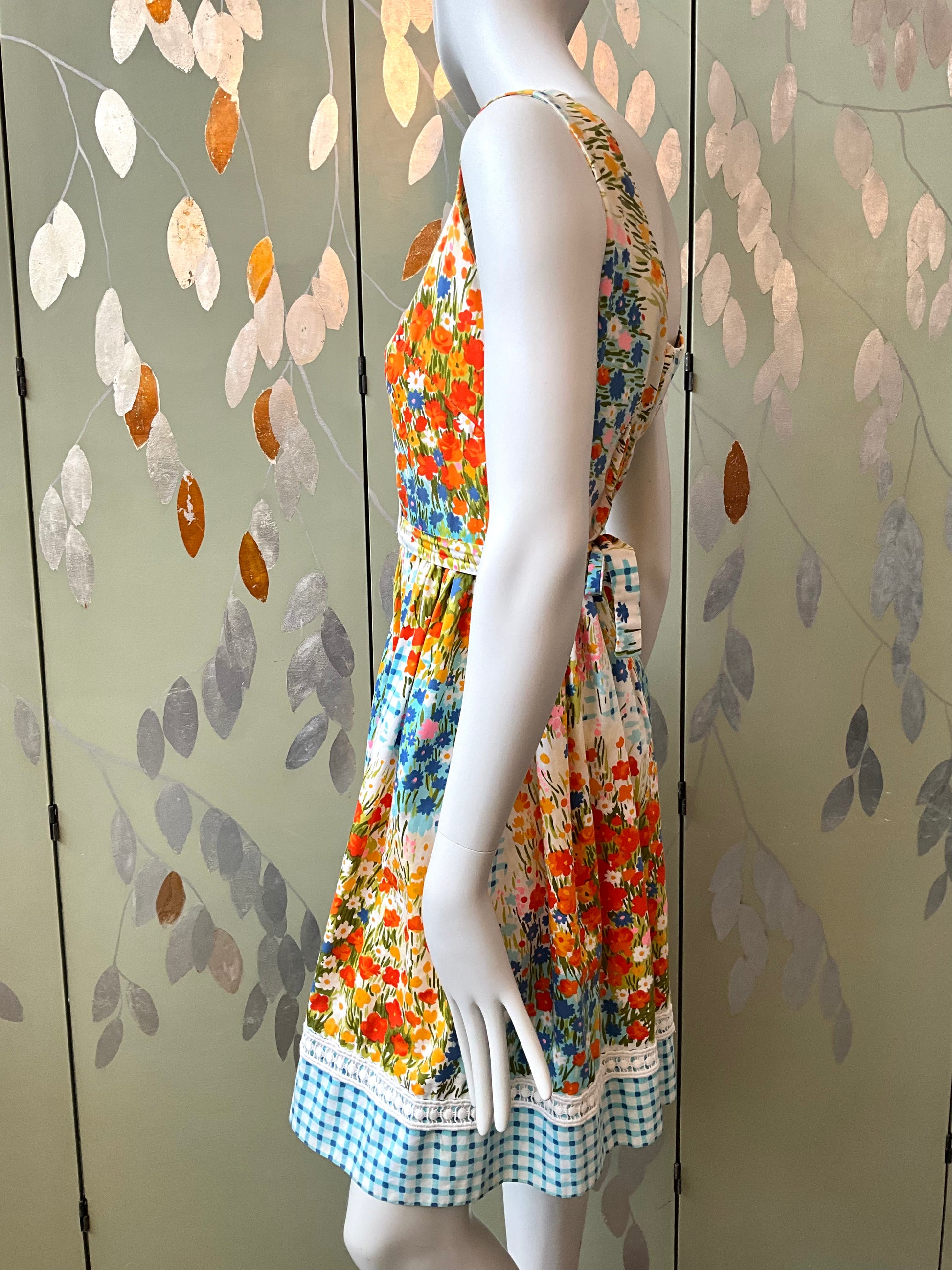 Mannequin wearing a colorful floral dress against a decorative wall.
