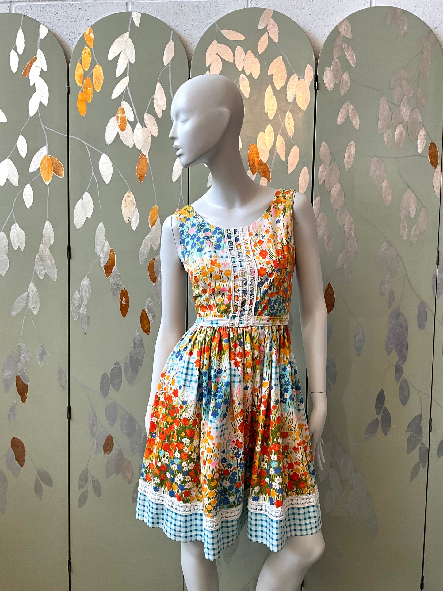 Mannequin wearing a colorful floral dress against a decorative screen with leaf patterns.