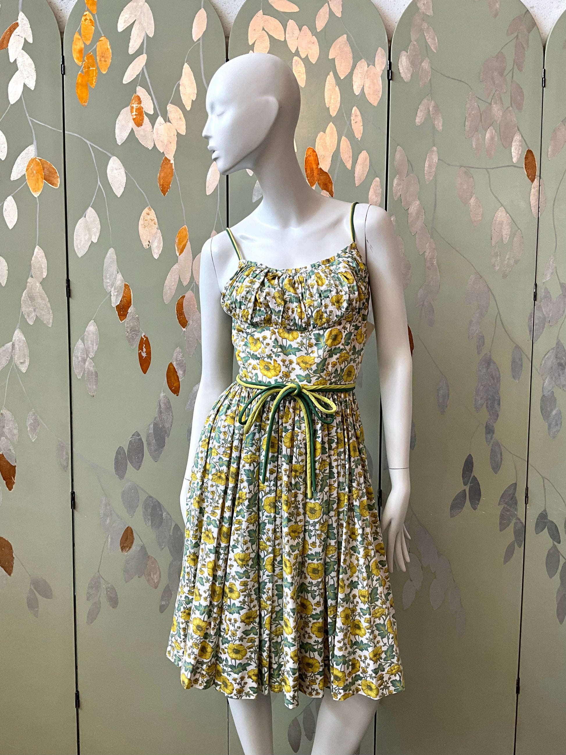 Mannequin wearing a floral dress against a decorative wall with leaf patterns.