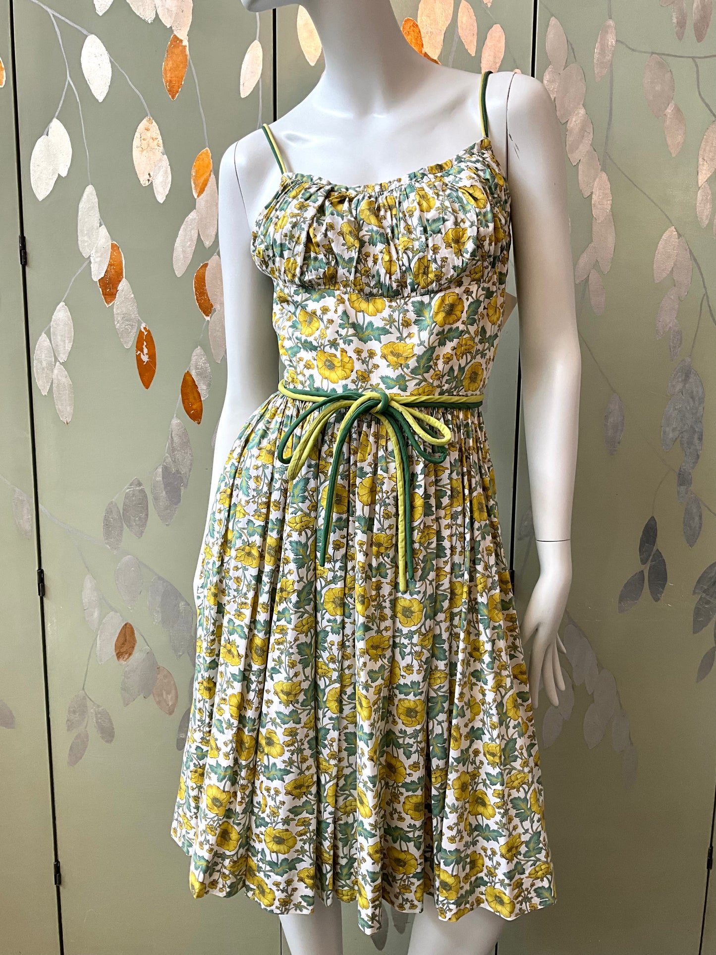 Floral dress on a mannequin against a decorative wall.