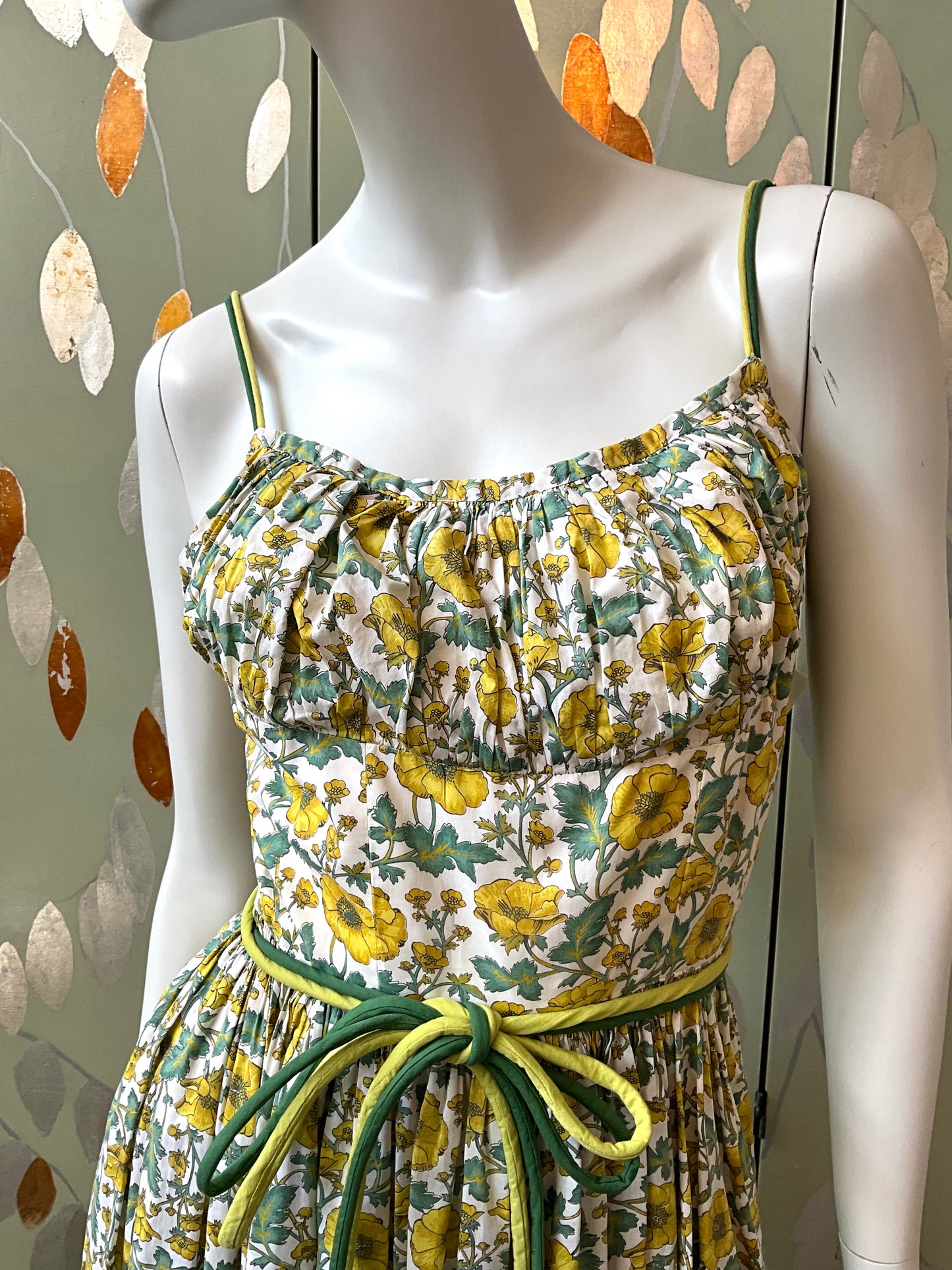 Floral dress with yellow and green accents on a mannequin against a decorative background.
