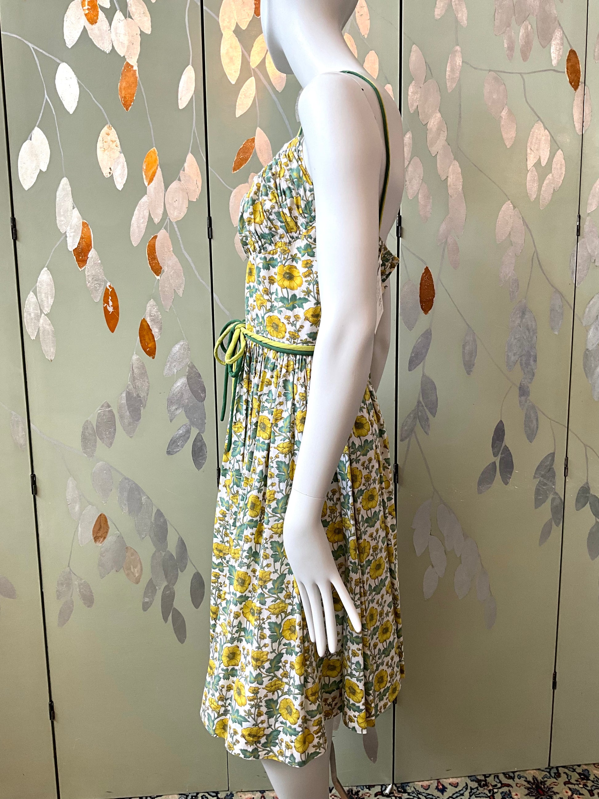 Mannequin wearing a floral dress against a decorative wall with leaf patterns.