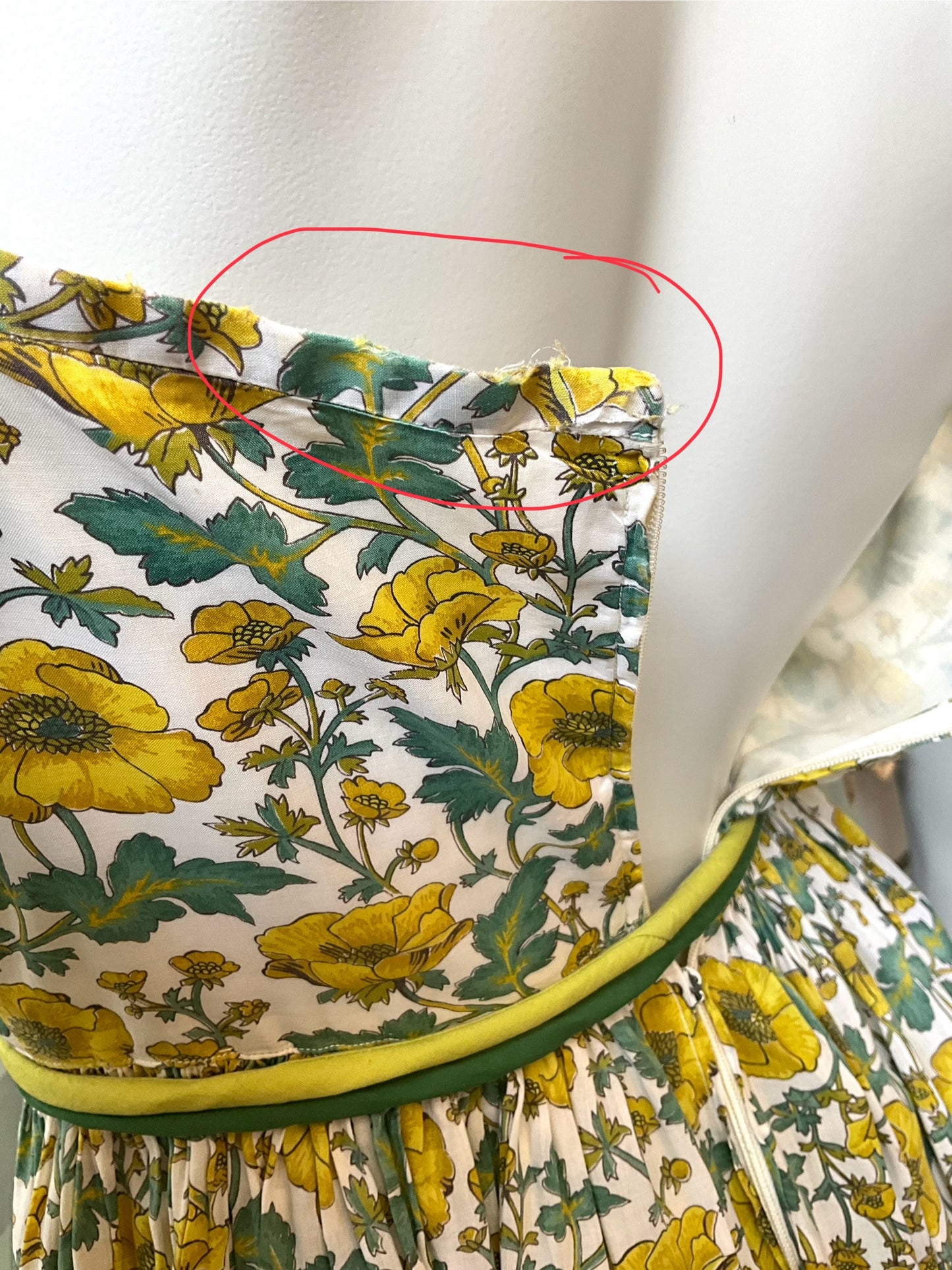 Close-up of a floral dress with yellow flowers and green leaves on a plain background.