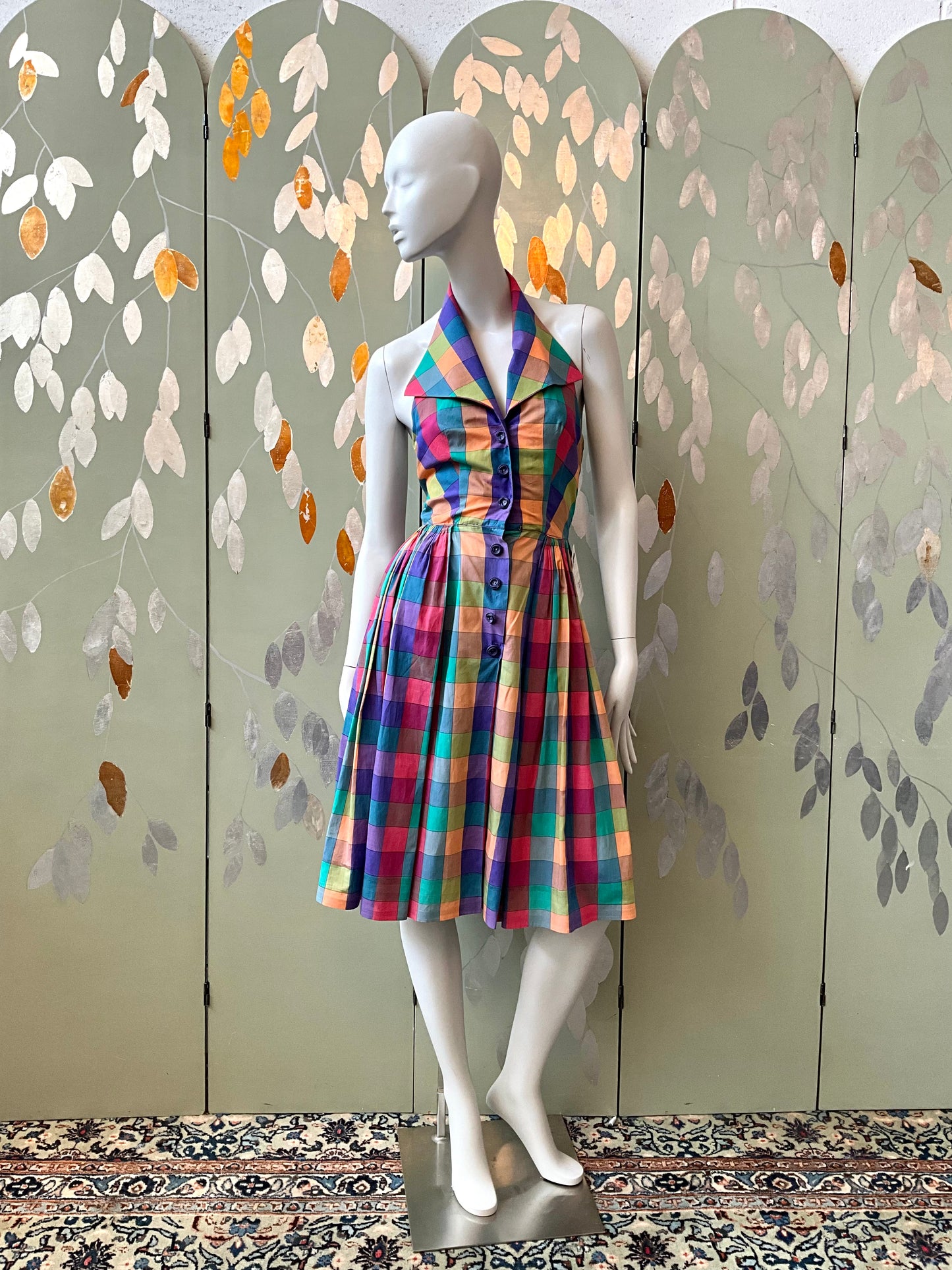 Mannequin wearing a colorful dress against a decorative wall with leaf patterns.