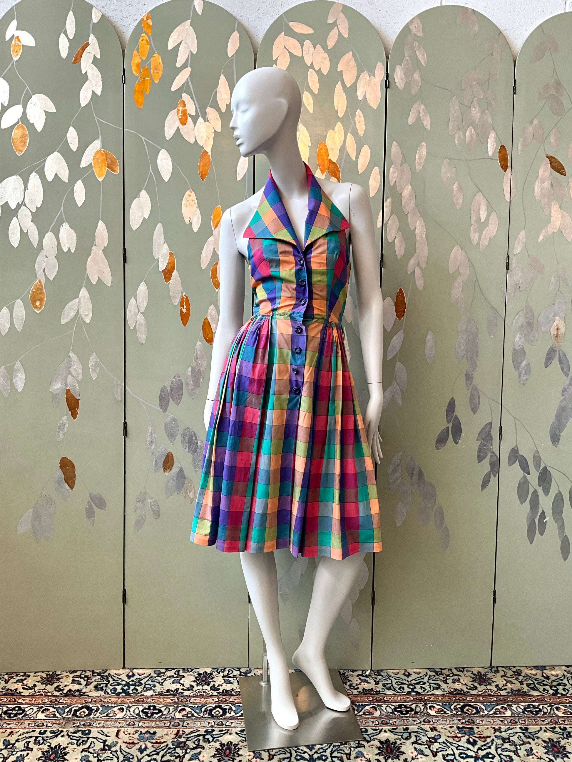 Mannequin wearing a colorful dress against a decorative wall with leaf patterns.