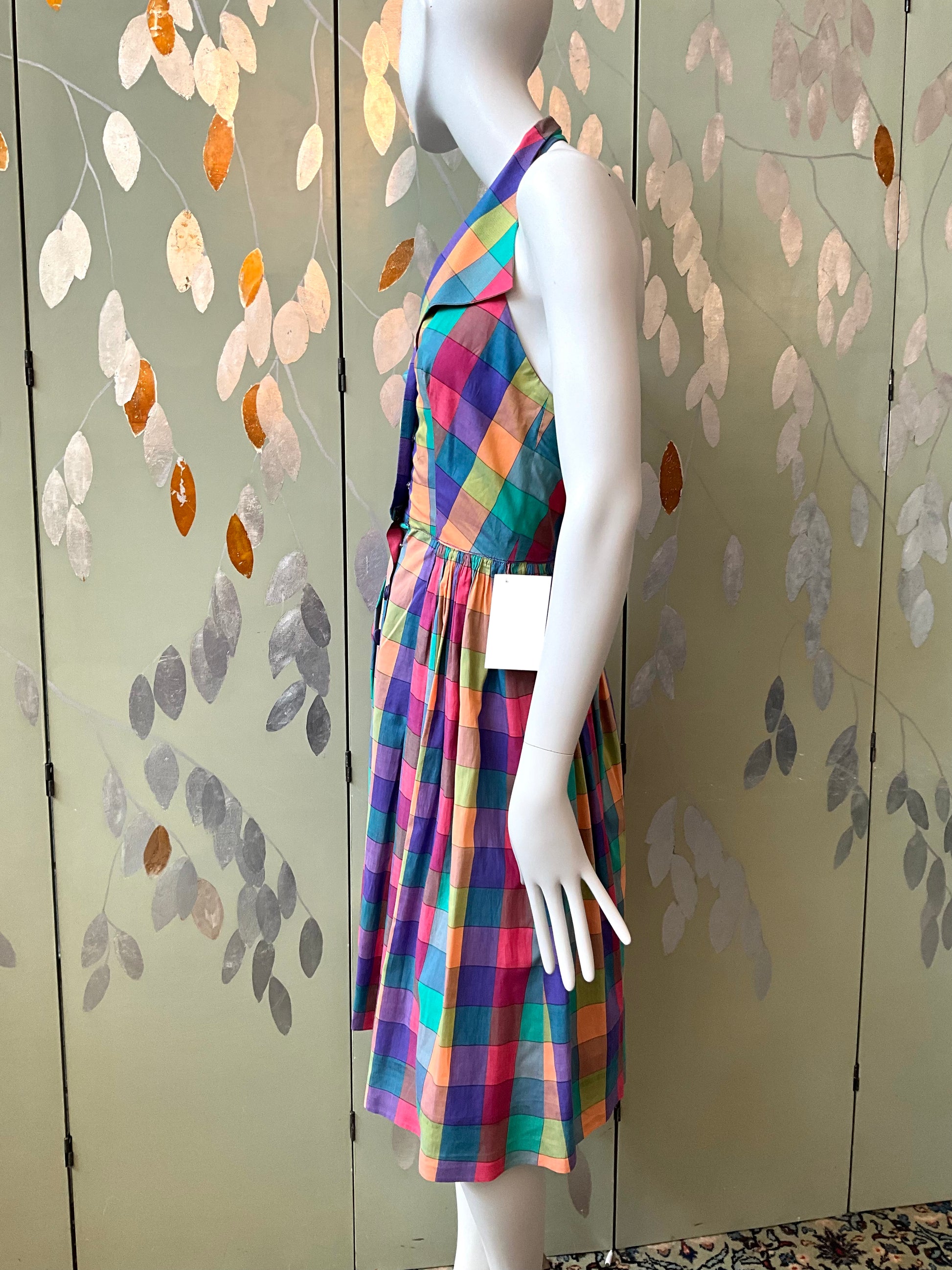 Mannequin wearing a colorful checkered dress against a decorative wall.