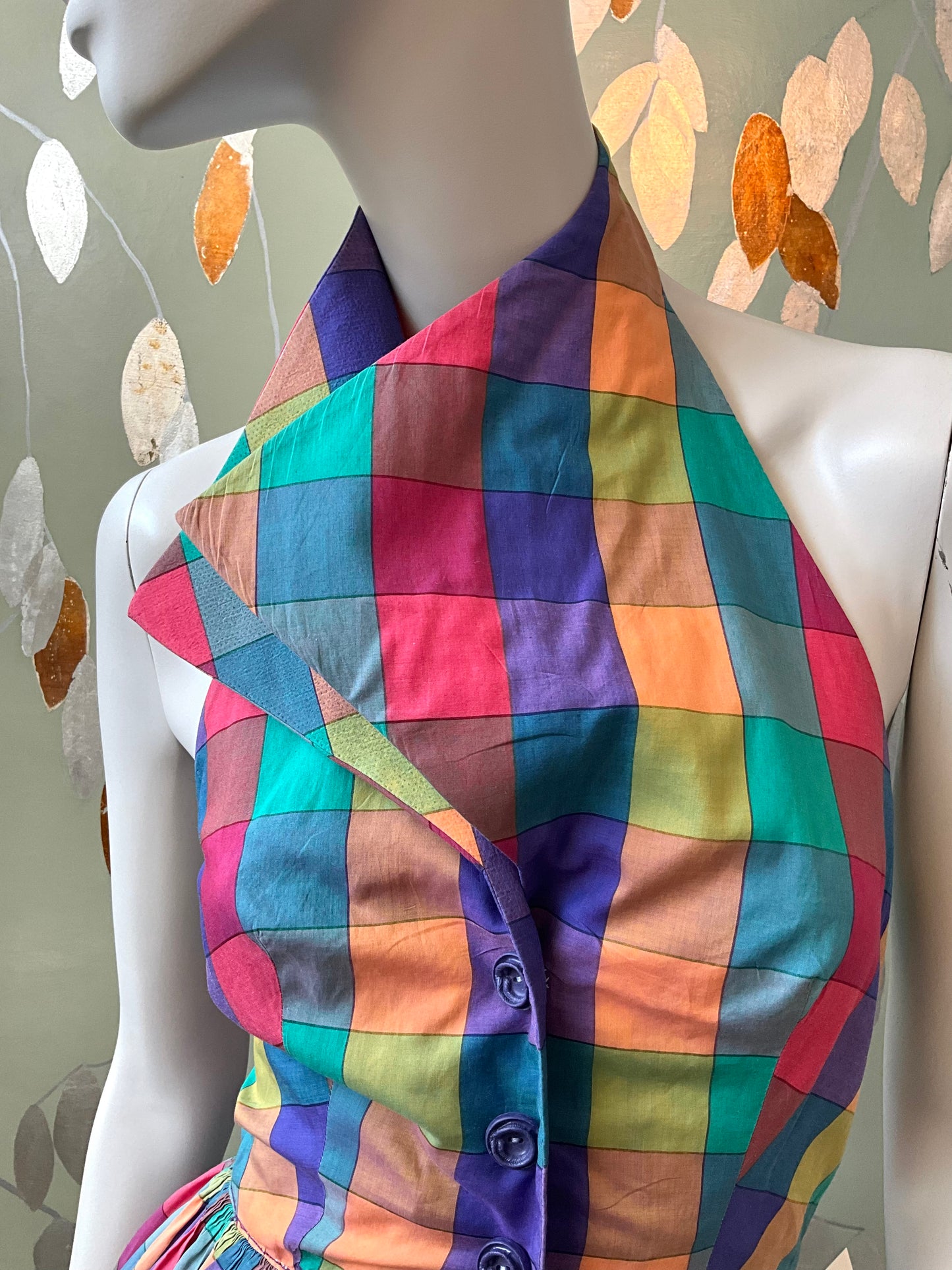 Mannequin wearing a colorful checkered dress with a leafy background
