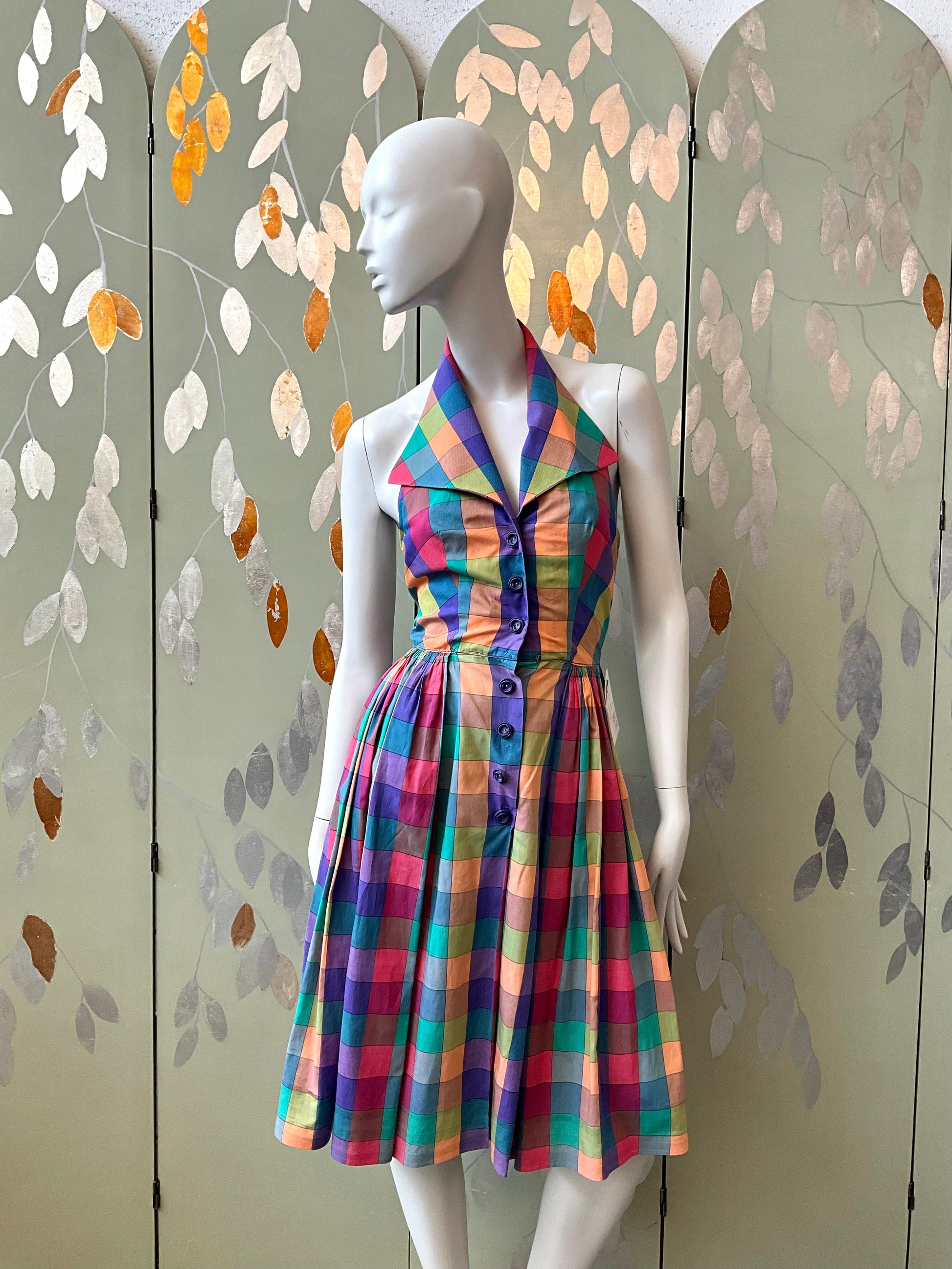 Mannequin wearing a colorful plaid dress against a decorative wall.