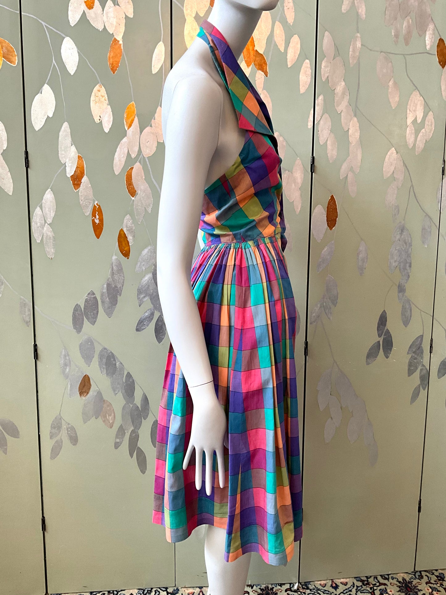 Mannequin wearing a colorful plaid dress against a decorative wall.
