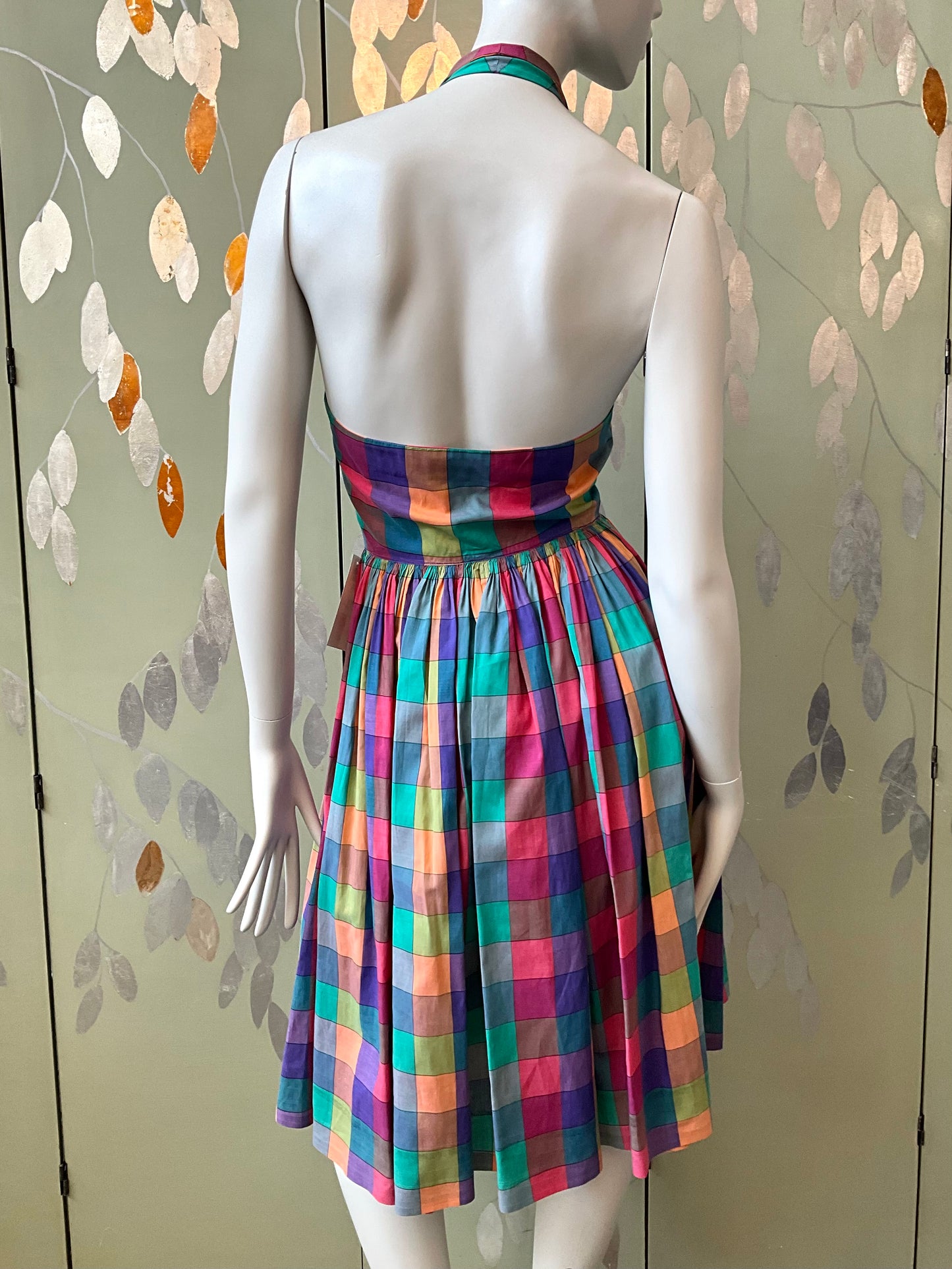 Mannequin wearing a colorful plaid dress against a patterned wall.