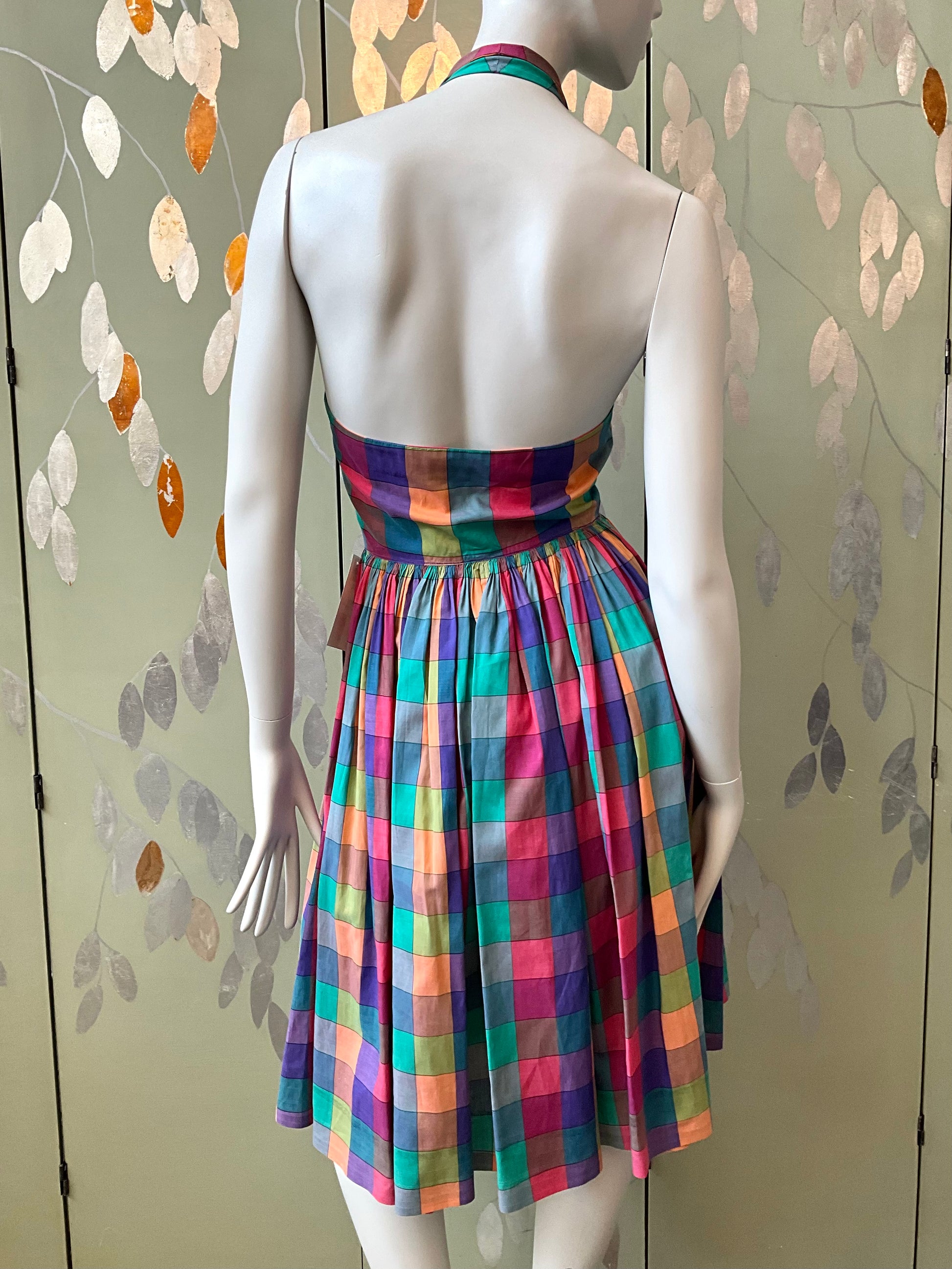 Mannequin wearing a colorful plaid dress against a patterned wall.