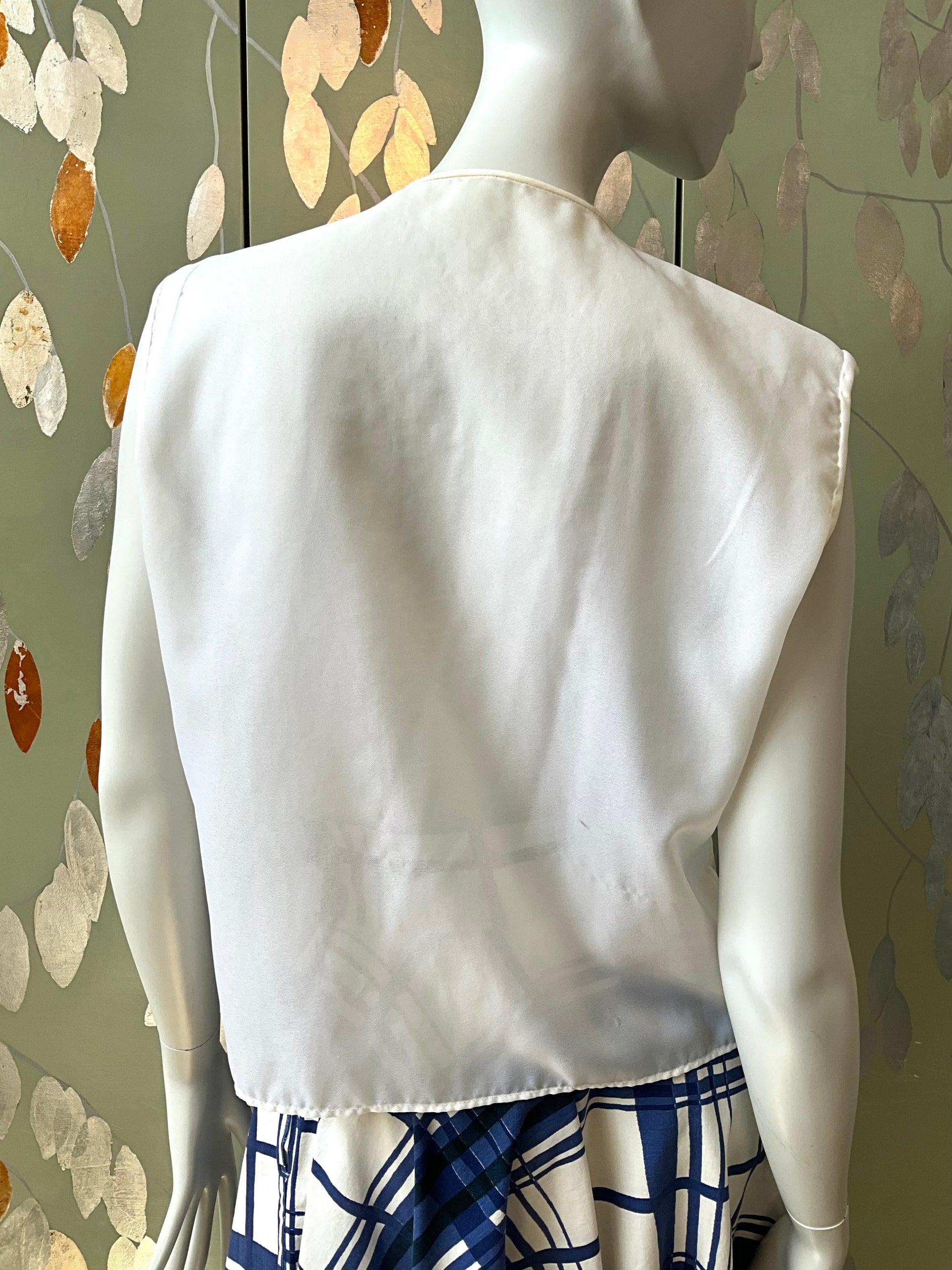 Mannequin wearing a white top with a patterned skirt against a decorative wall.