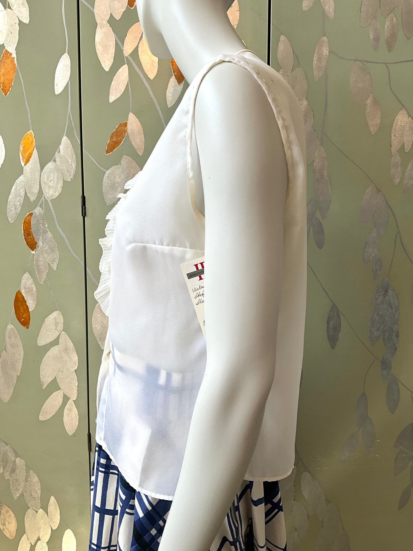 White blouse on a mannequin against a leaf-patterned wall