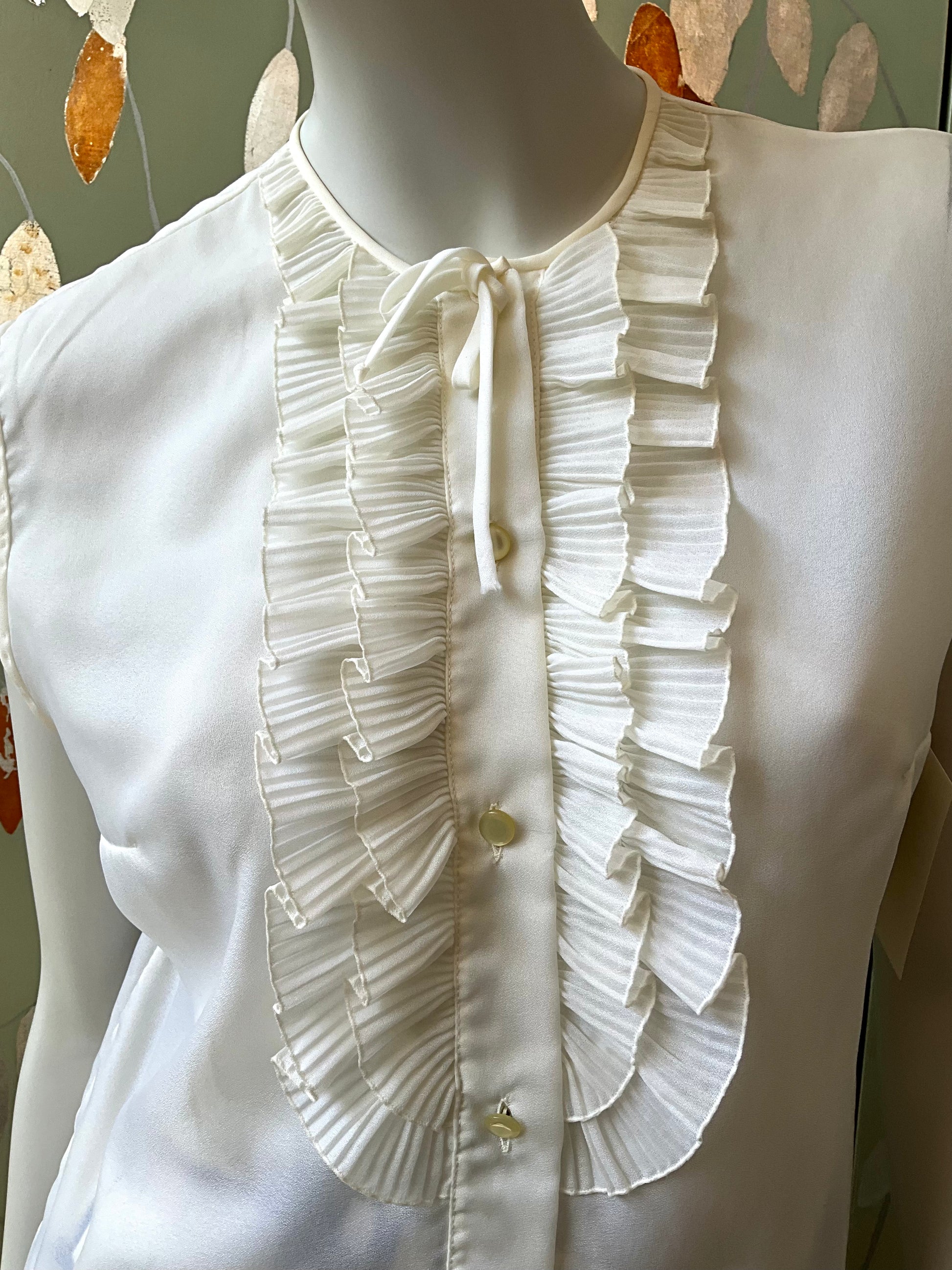 White blouse with ruffled details on a mannequin against a neutral background