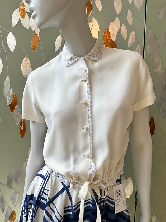 Mannequin wearing a white blouse with lace details against a decorative wall.