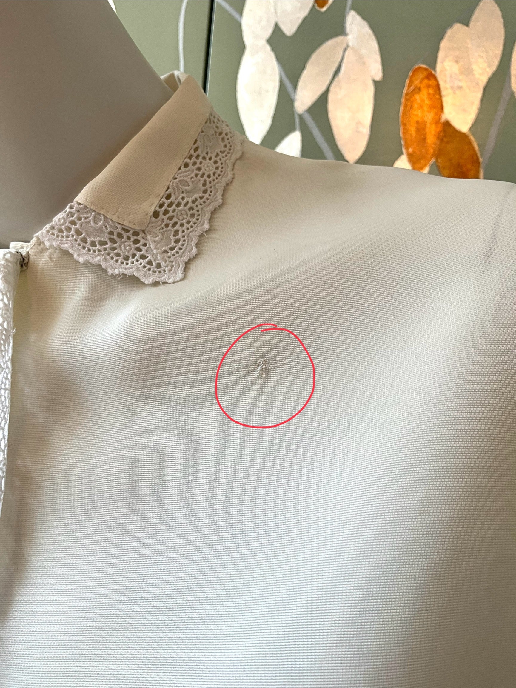 White blouse with lace collar on a mannequin, with a red circle highlighting a small imperfection.