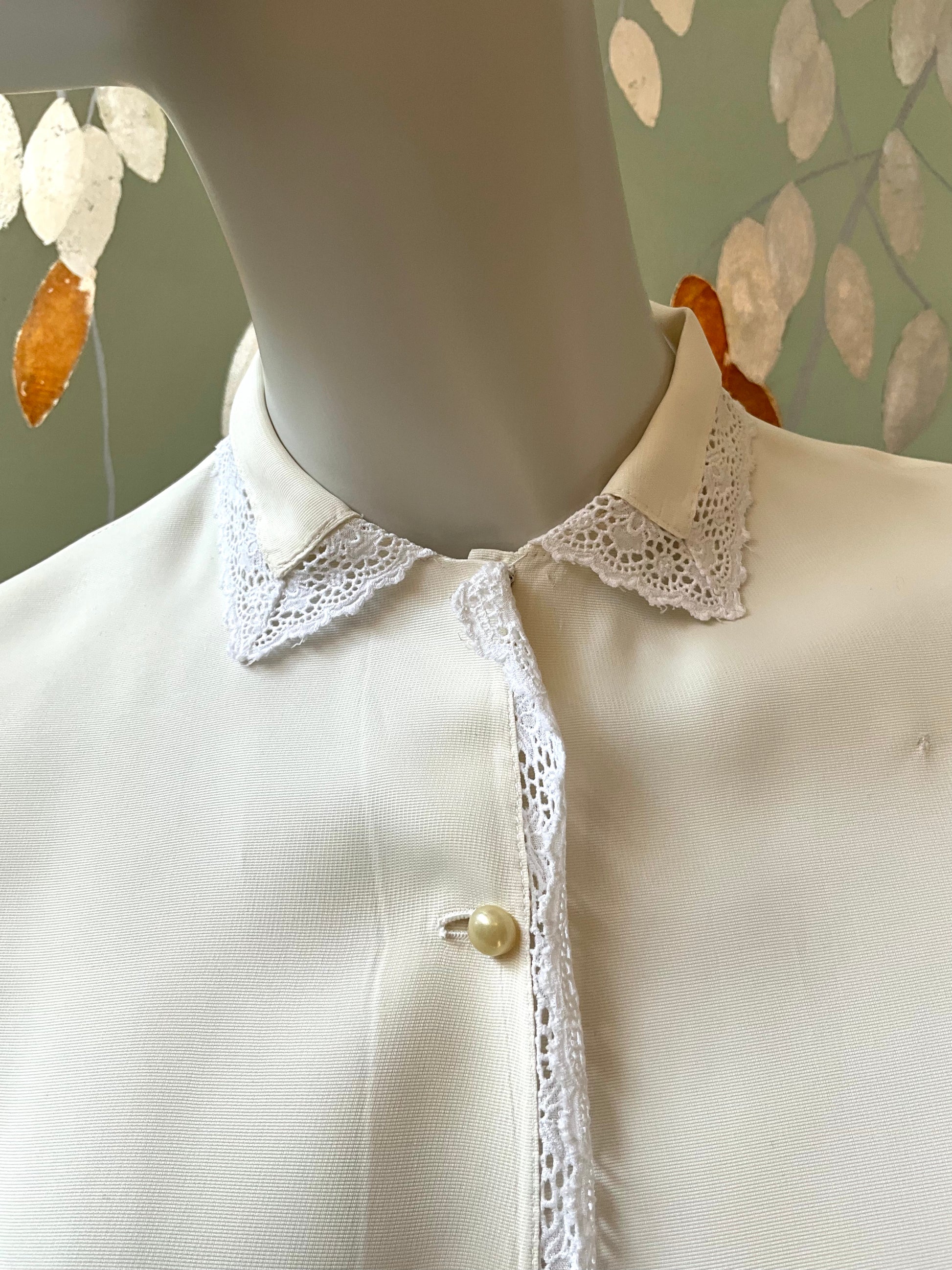 White blouse with lace collar on a mannequin against a leaf-patterned wall.