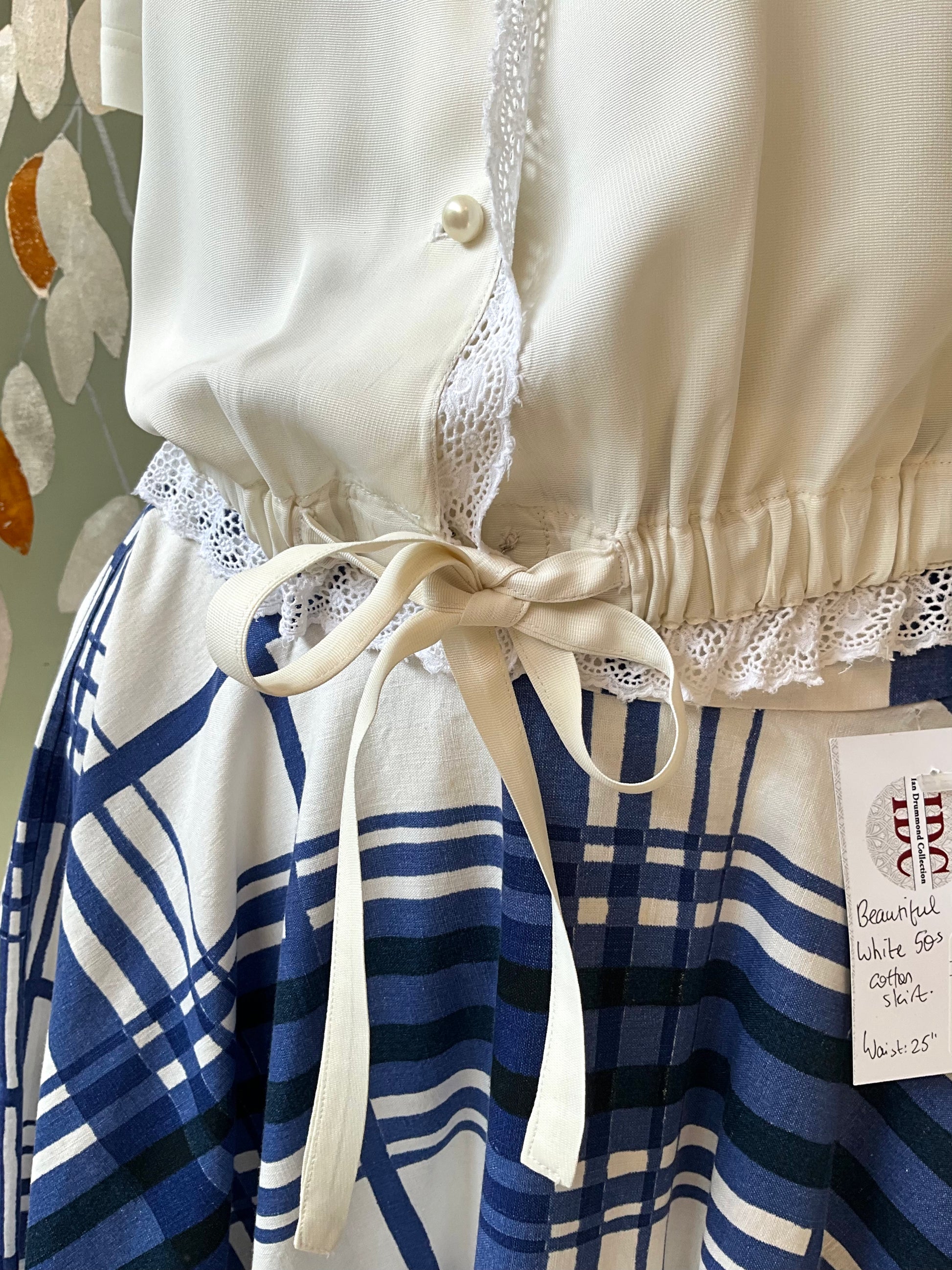 White blouse with lace trim and blue plaid skirt on a neutral background