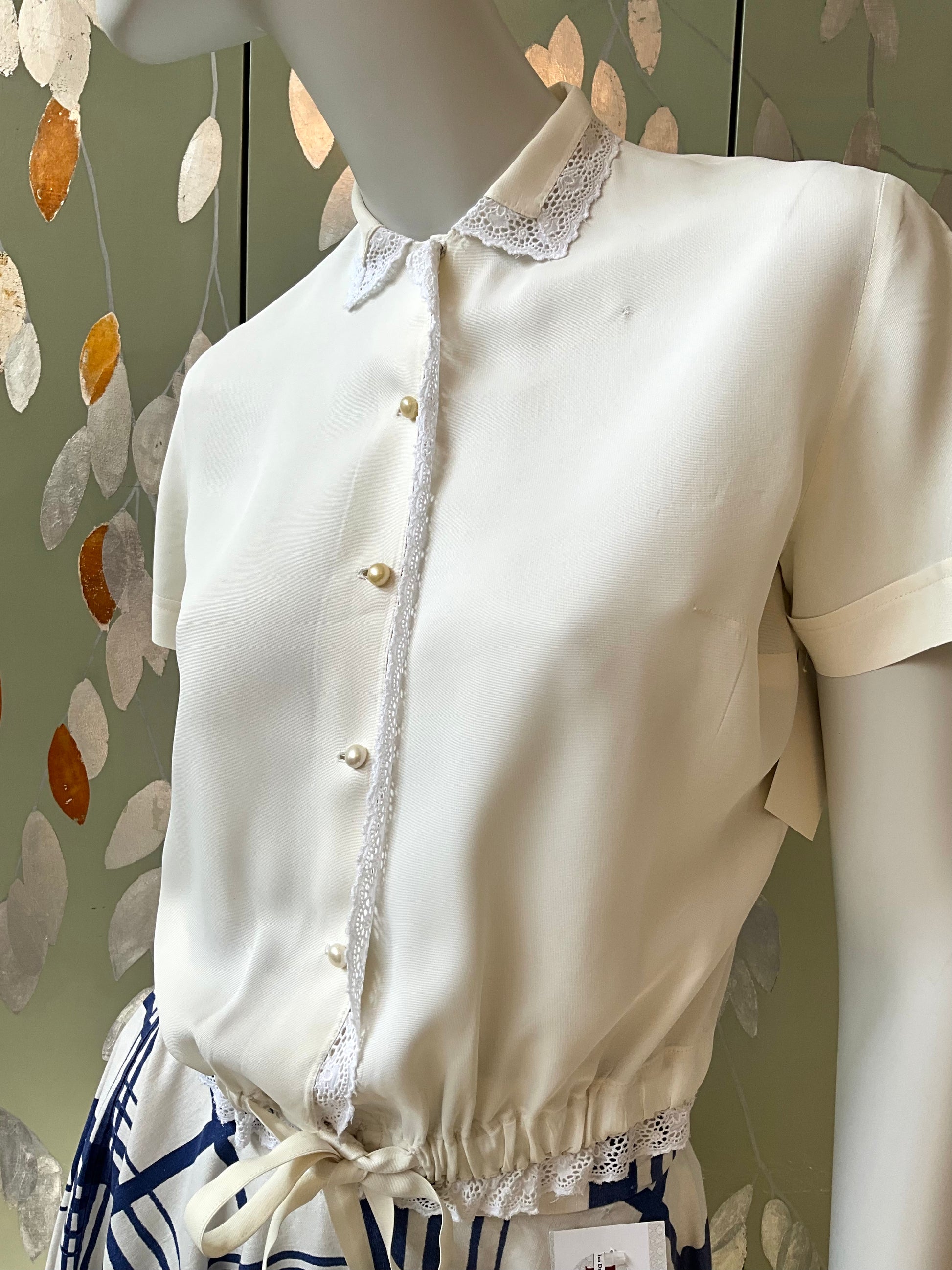 White blouse with lace details on a mannequin against a decorative wall.