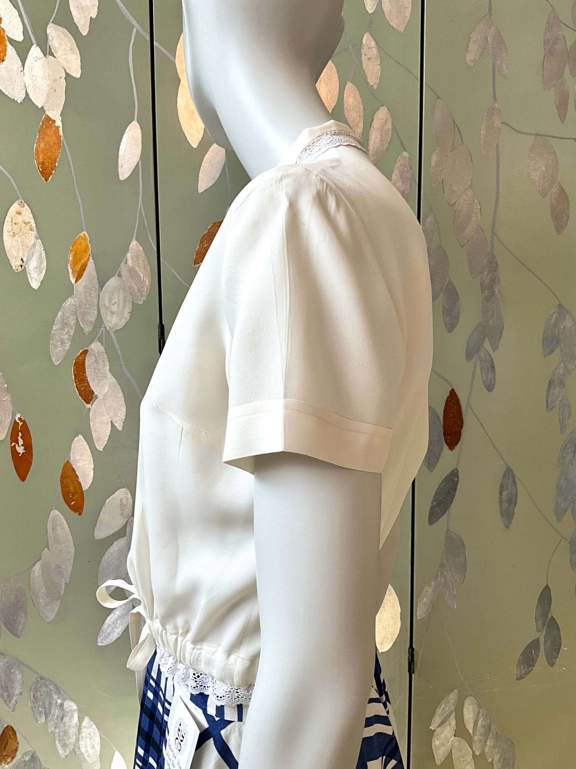 Mannequin wearing a white blouse against a decorative wall.