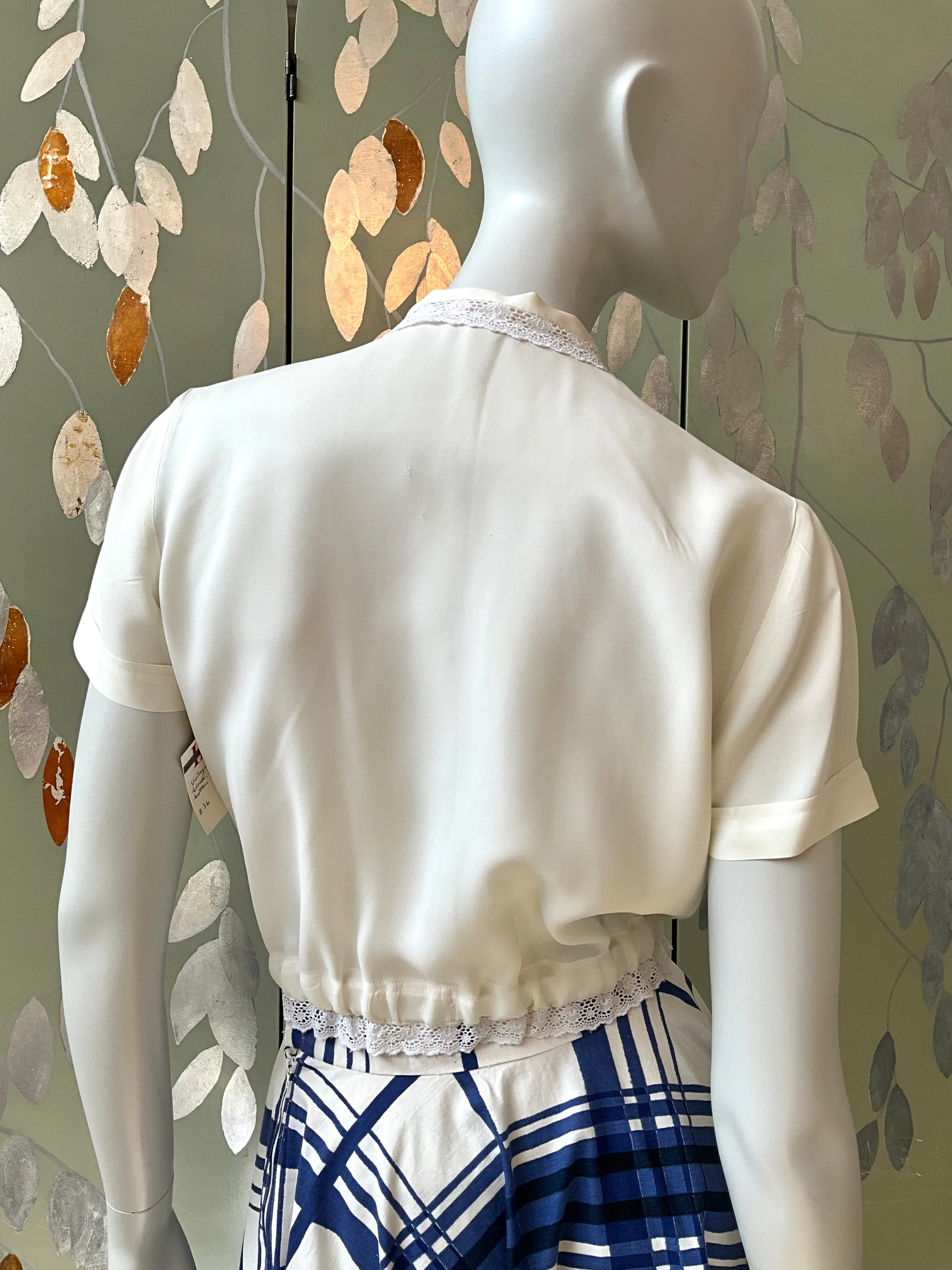 Mannequin wearing a white top with lace details against a decorative wall.