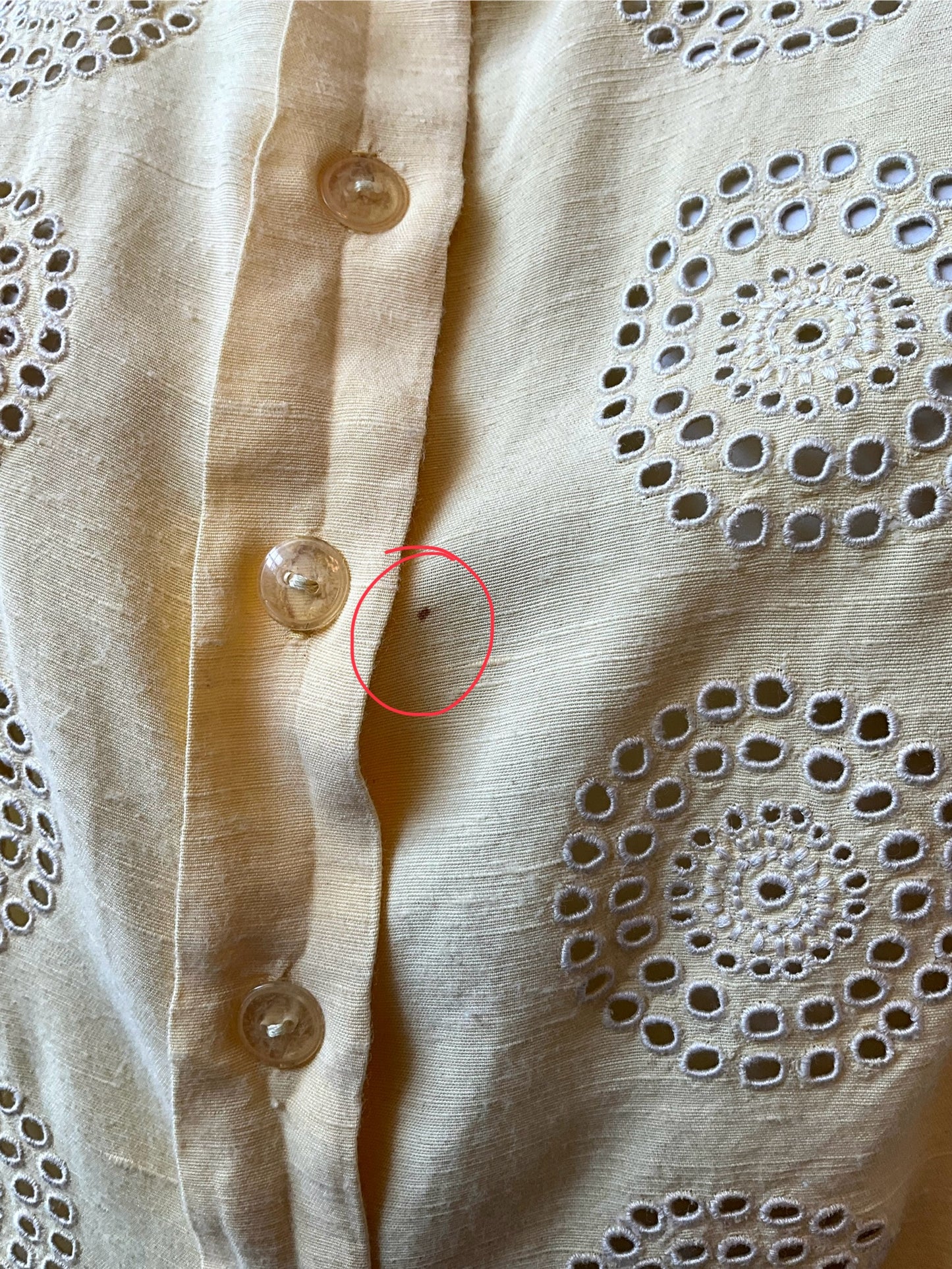 Close-up of a yellow fabric with button details and a red circle highlighting a small defect.