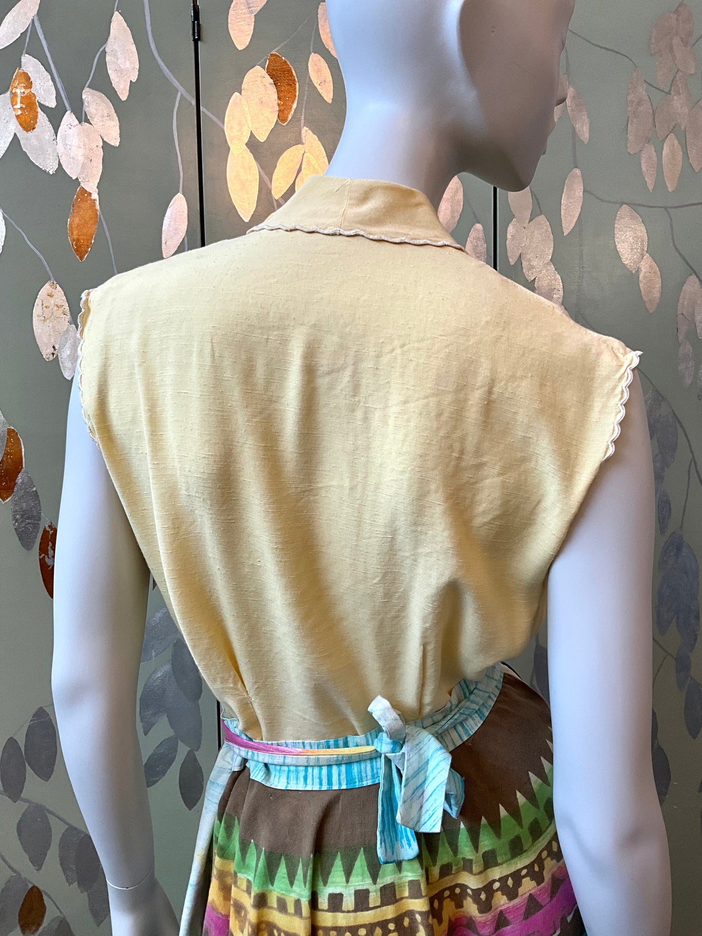 Mannequin wearing a yellow sleeveless top with a patterned skirt in front of a decorative wall.