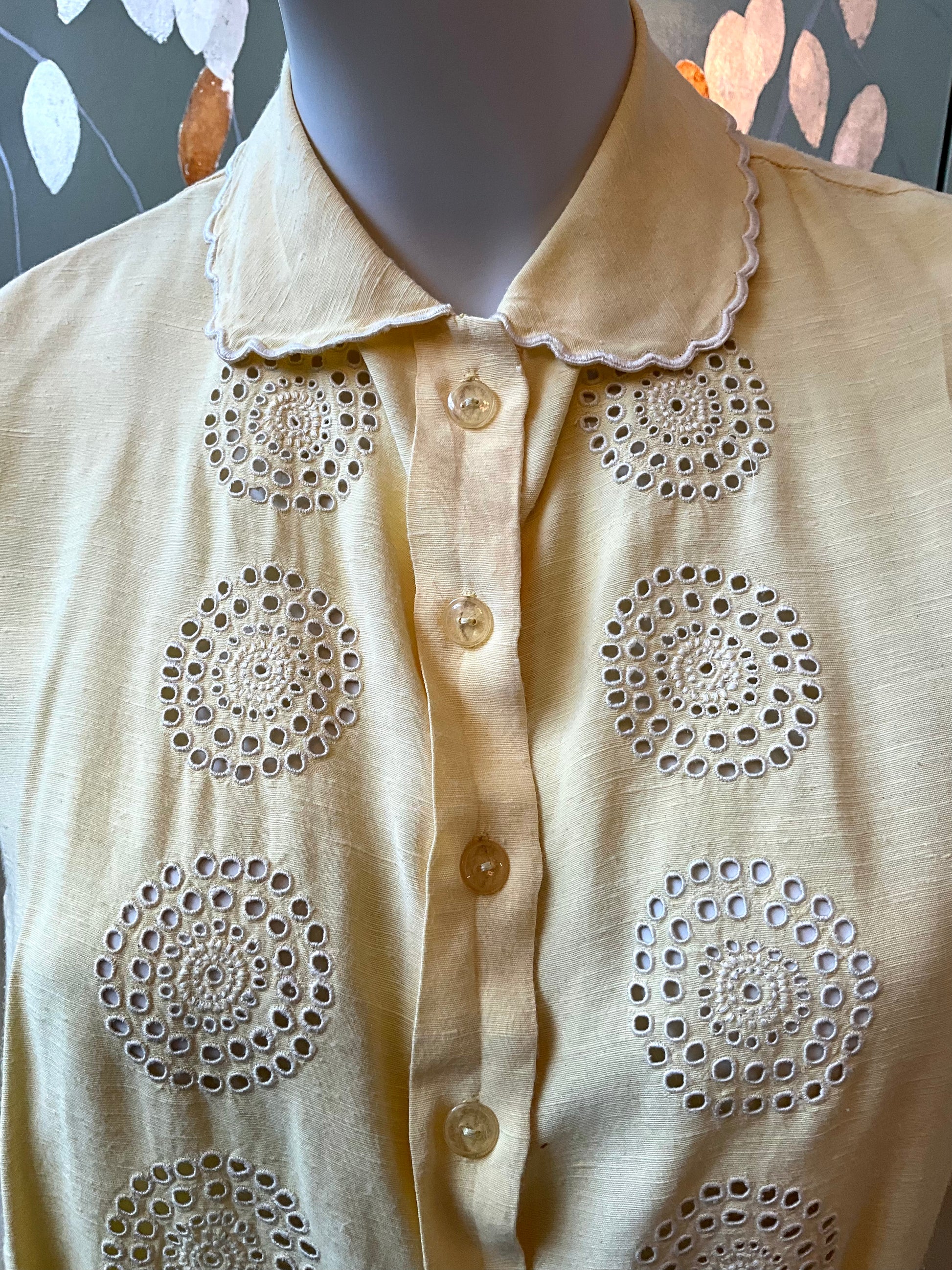 Yellow blouse with decorative cut-out patterns on a mannequin against a neutral background