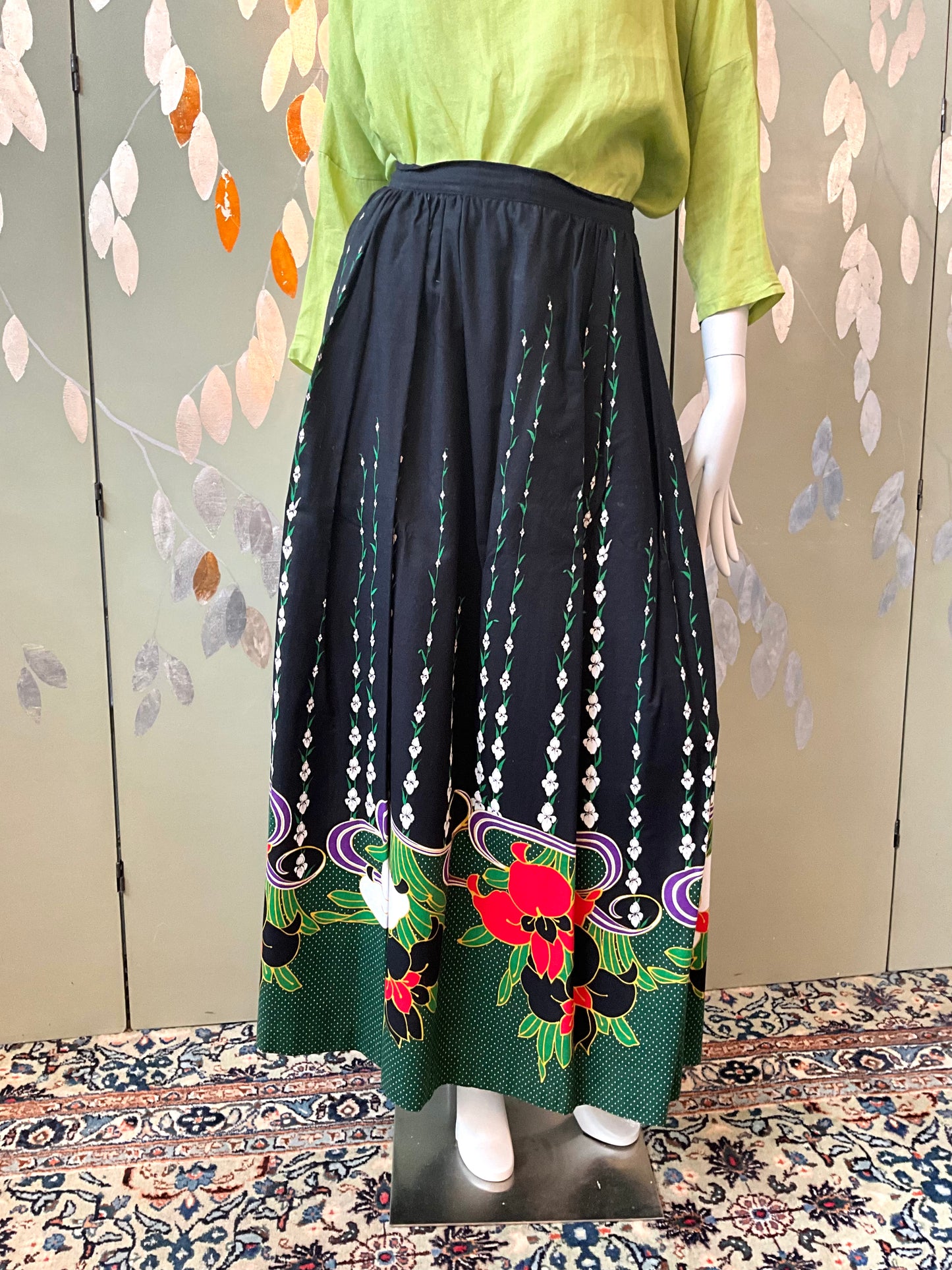 Mannequin wearing a green top and black skirt with floral patterns on a patterned floor.